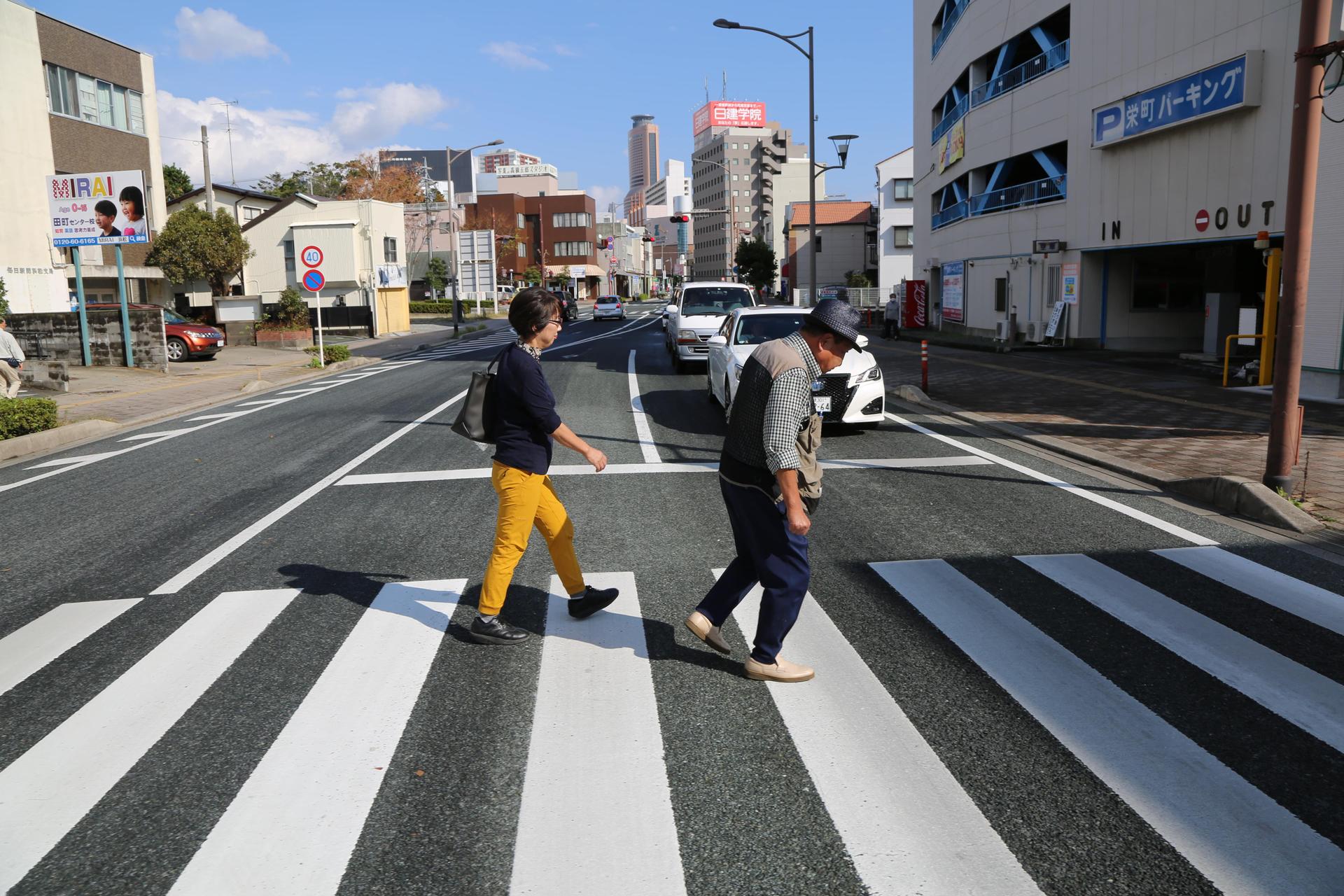a volunteer follows Iwao Hakamada as he walks across the street