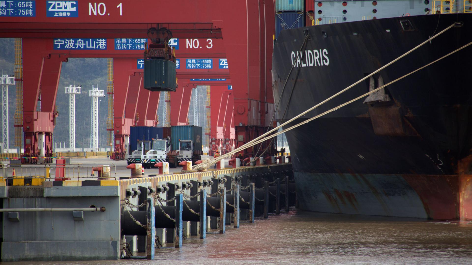 Trucks transport containers are shown being moved from trucks to a container ship at a port in China.