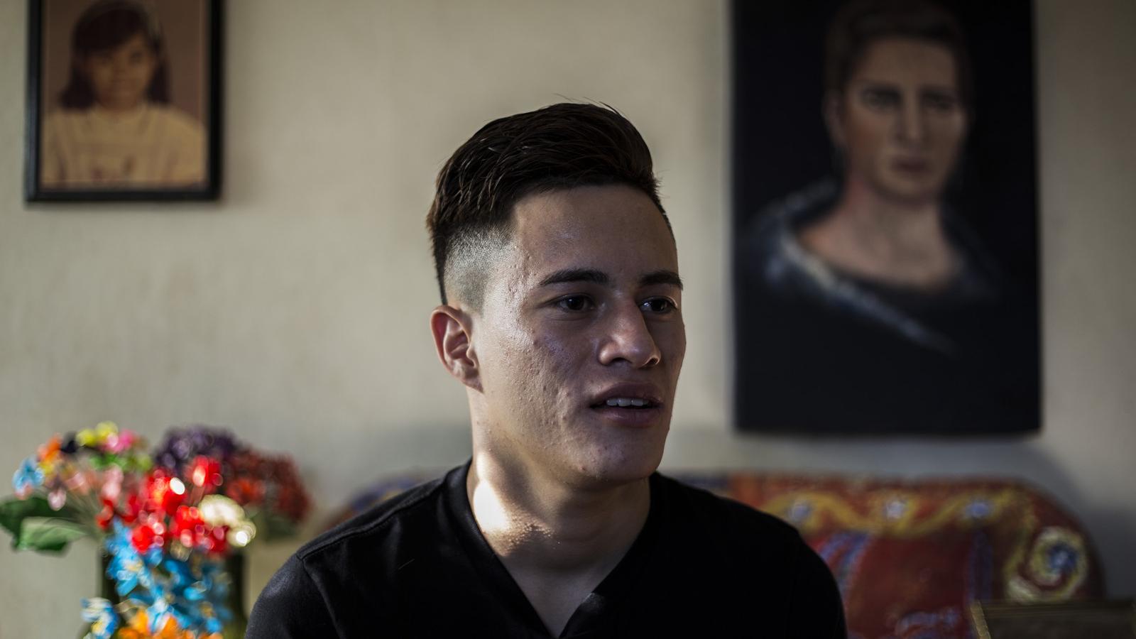 Daniel Alemán wears a black shirt in a room with two paintings on the wall and a blurry bouquet of flowers. 
