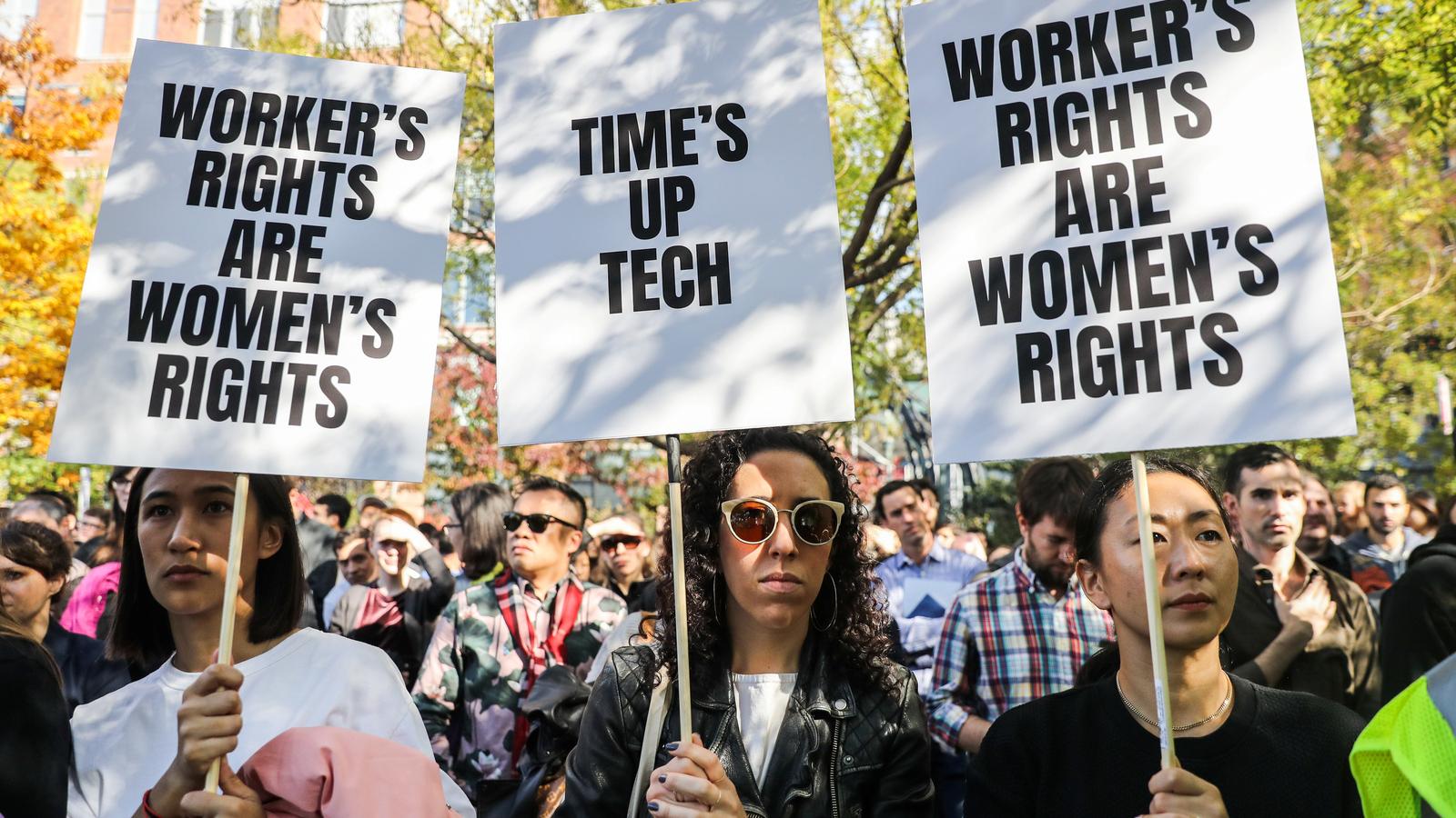 Three female Google workers hold protest signs with black lettering.
