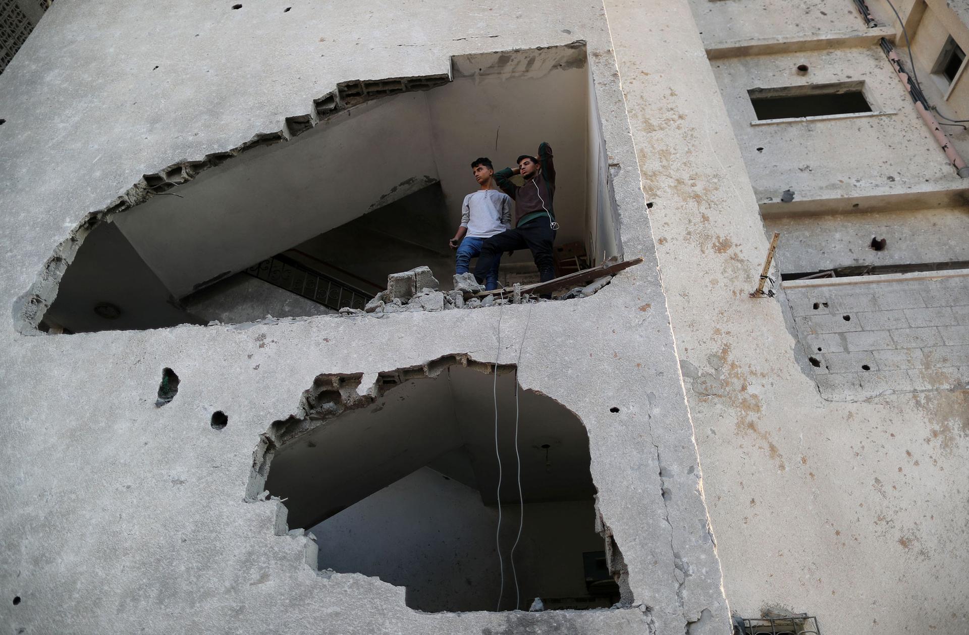Palestinians look out of their house through a large hole in the wall created from an Israeli air strike.