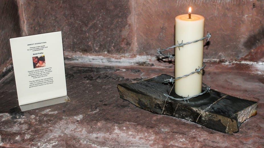 A candle surrounded by barbed wire next to a written description of Amal Fathy