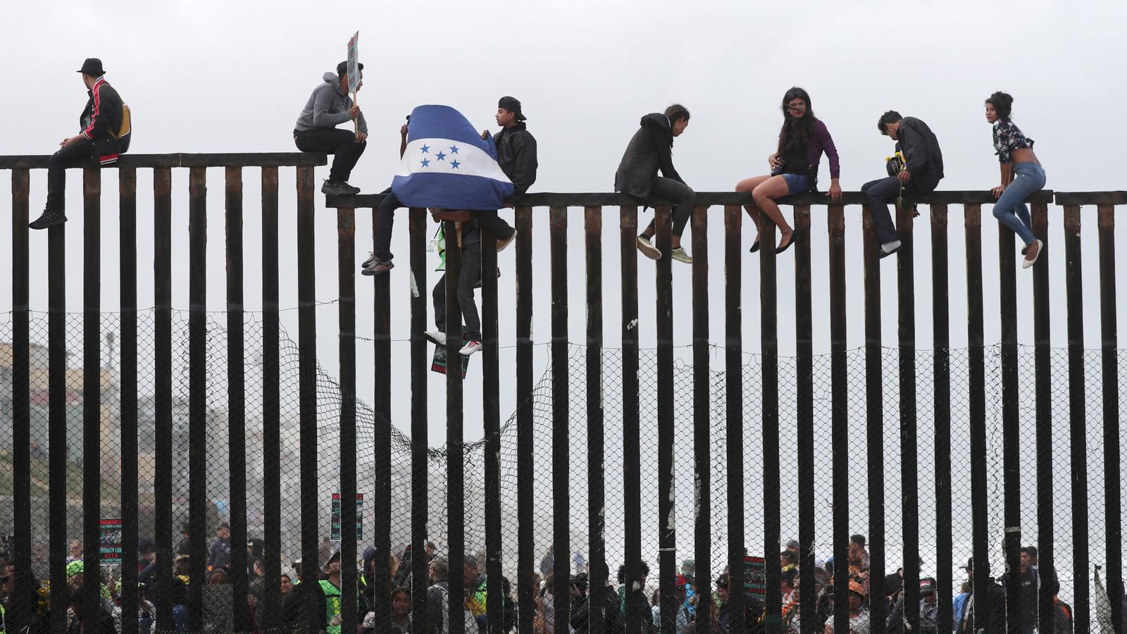 Migrants sit on top of the US-Mexico border wall. 
