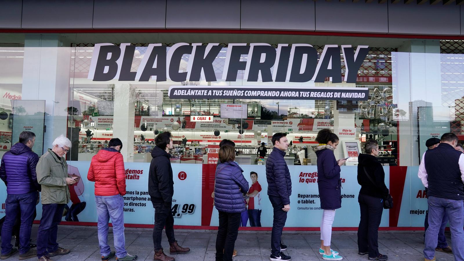 Shoppers wait in long lines in front of a storefront window that reads "Black Friday" in black and white letters.