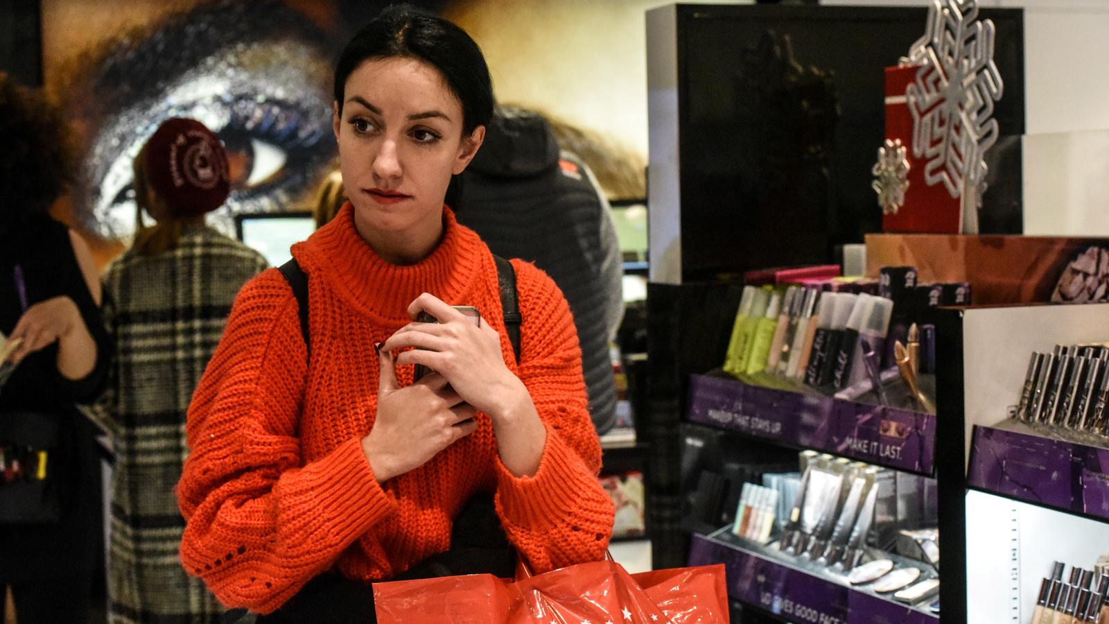 A woman wearing red sweater grips her phone at Macy's while shopping on Black Friday.