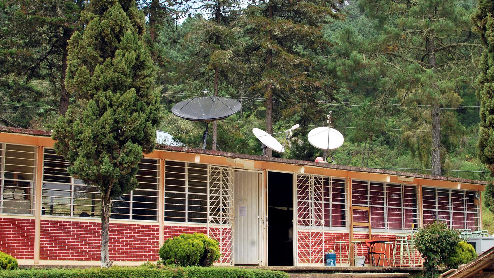 Satellites on the roof of a red brick school in Oaxaca state surrounded by green trees.