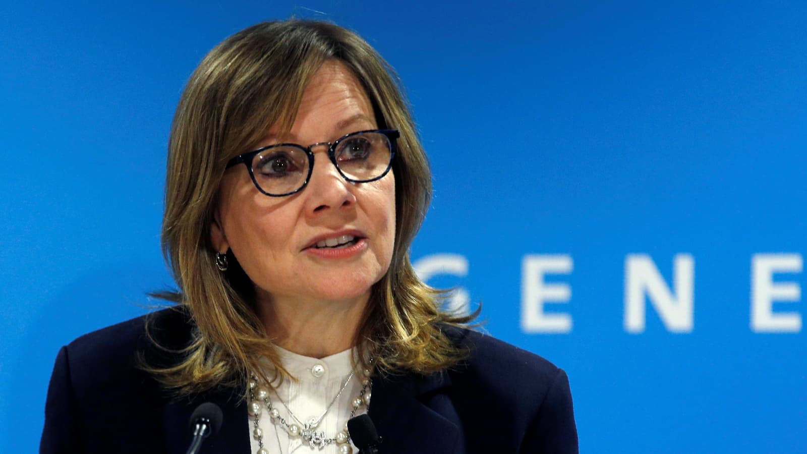 General Motors CEO Mary Barra at a press conference with a blue background.
