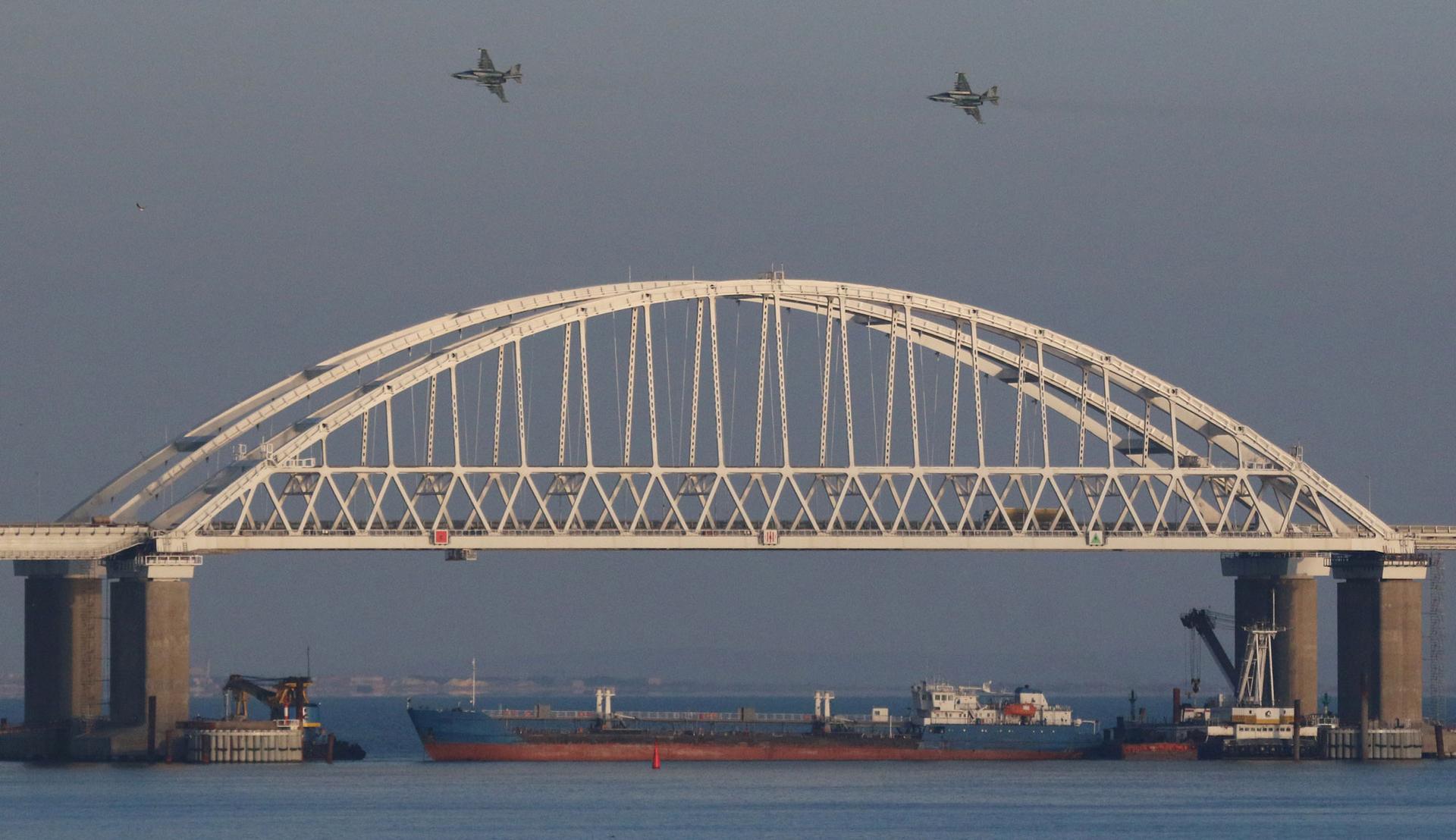 Russian jet fighters fly over a bridge connecting the Russian mainland with the Crimean Peninsula with a cargo ship beneath it
