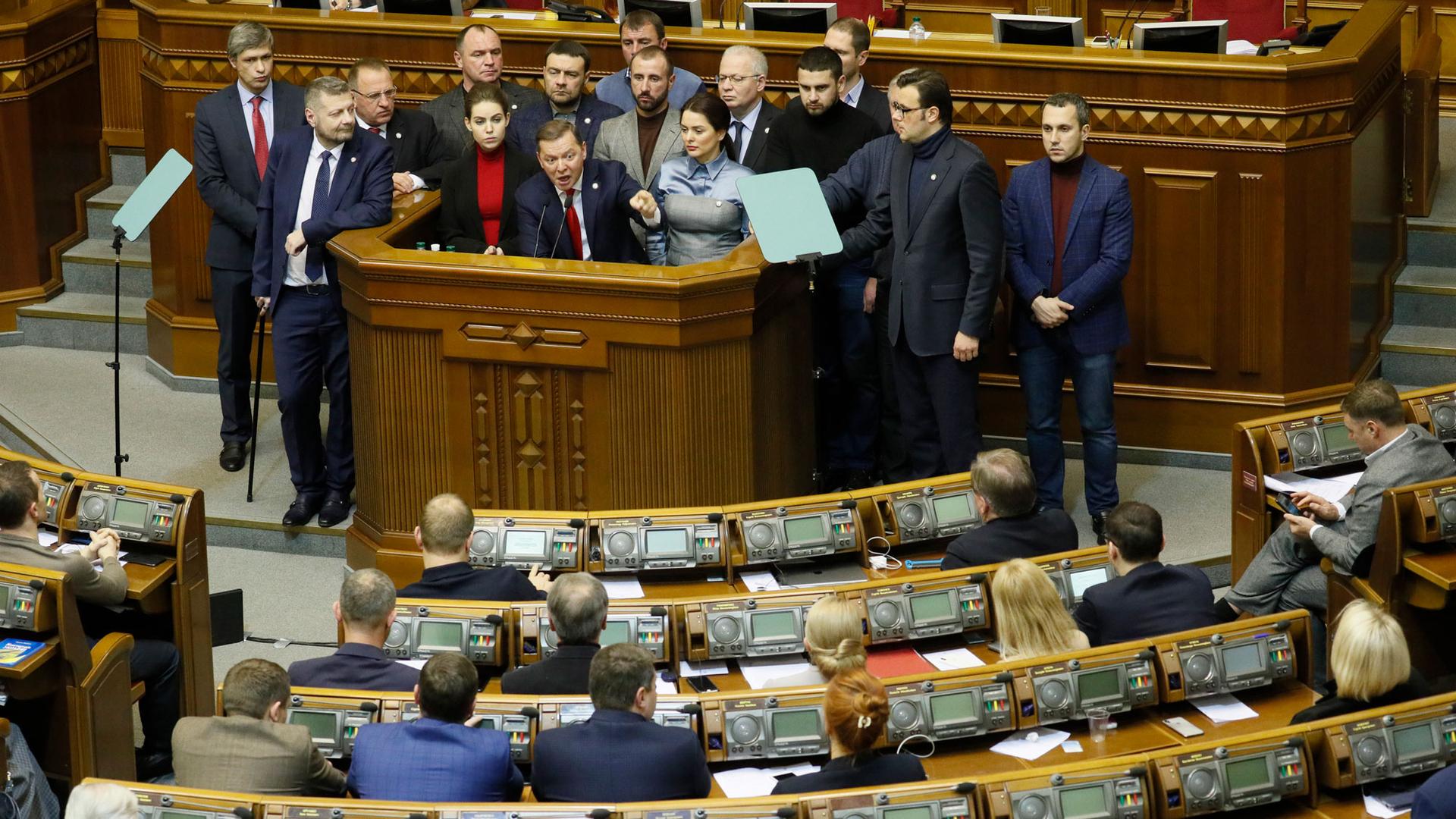 Ukrainian politician Oleh Lyashko is shown with several people behind standing at a podium pointing his finger during a parliament session.