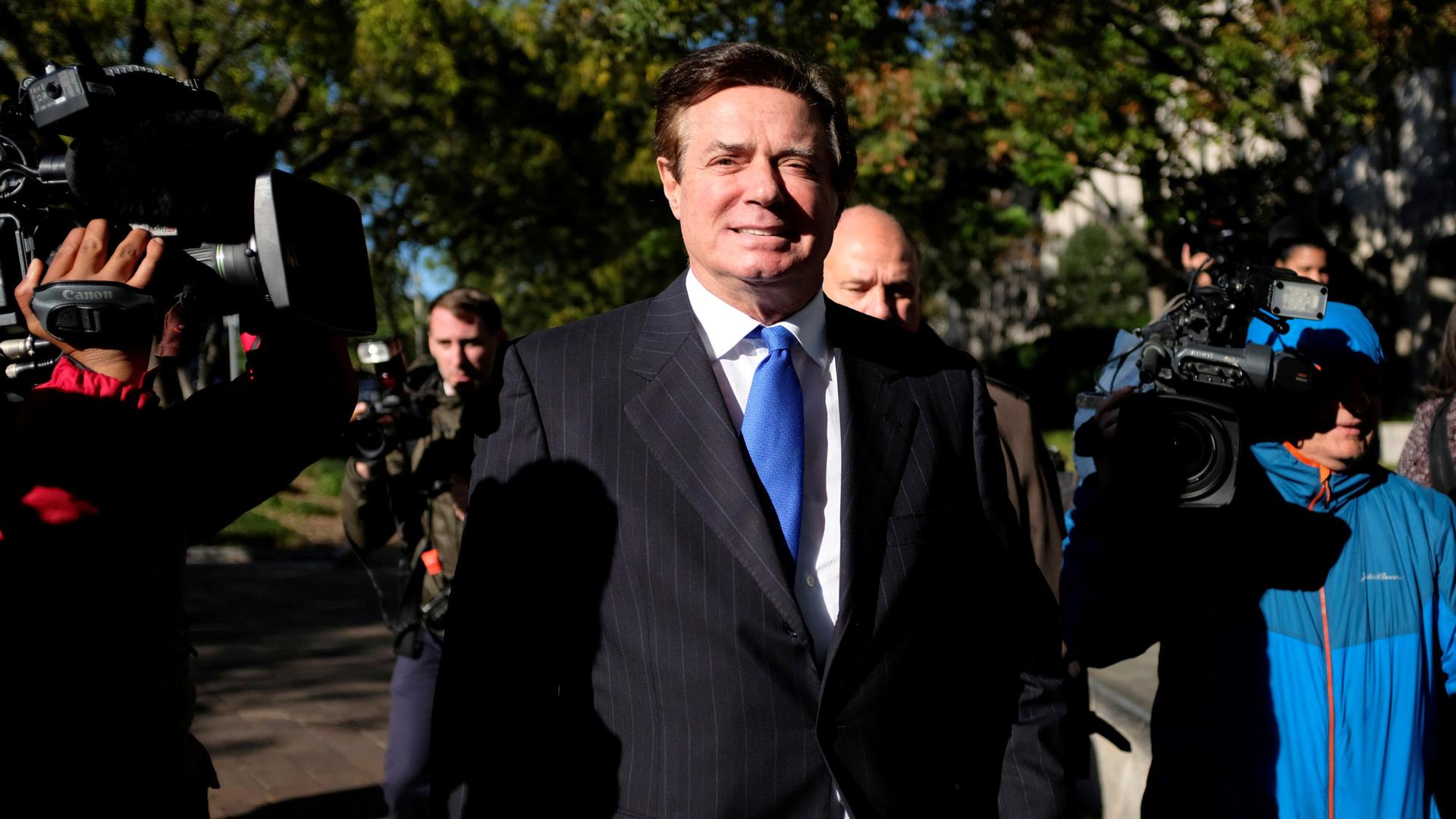 Former Trump 2016 campaign chairman Paul Manafort is shown wearing a suit and blue tie surrounded by cameras in Washington, 2017.