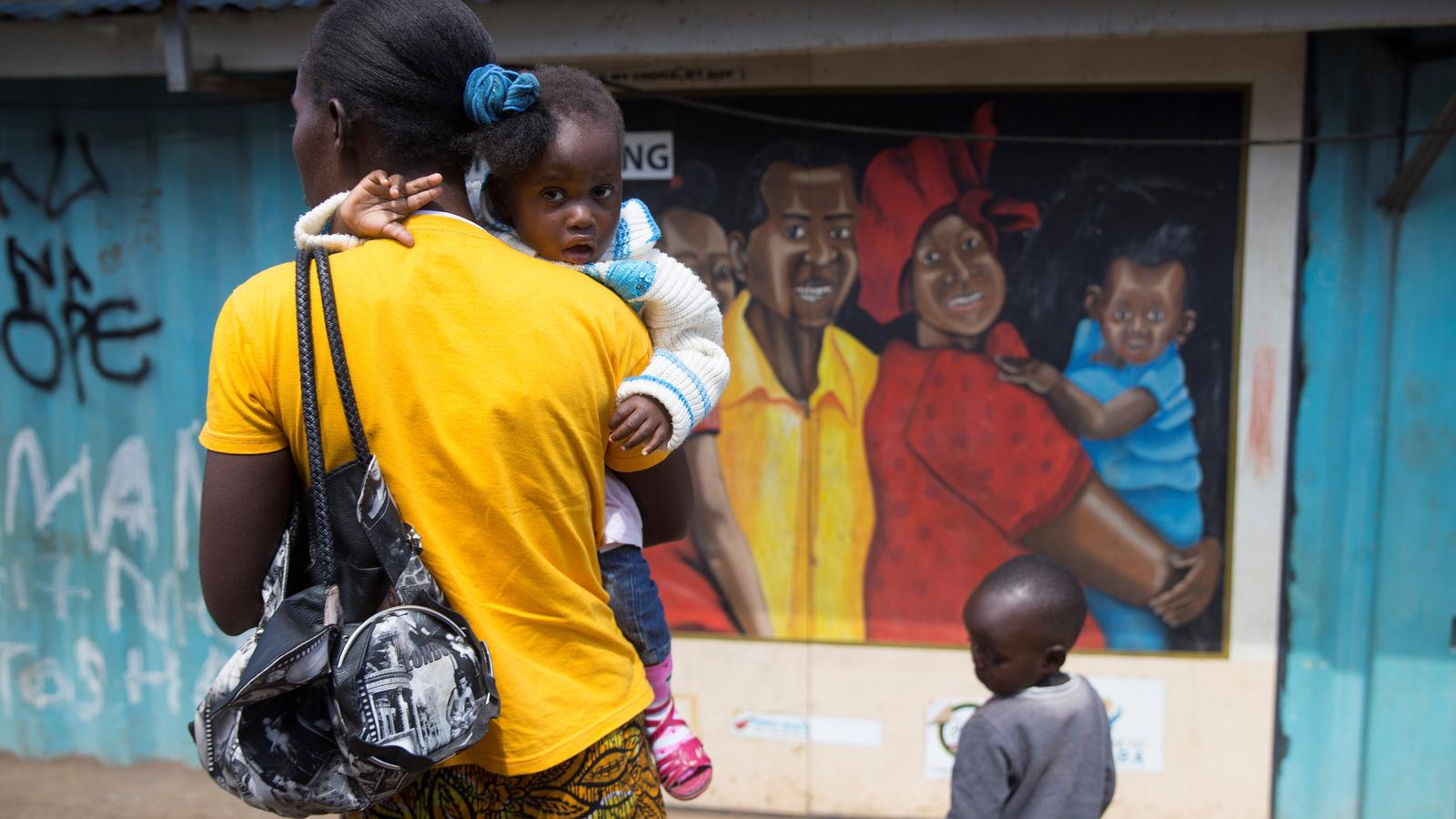 A woman wearing a yellow shirt holds a toddler in her arms near a mural.