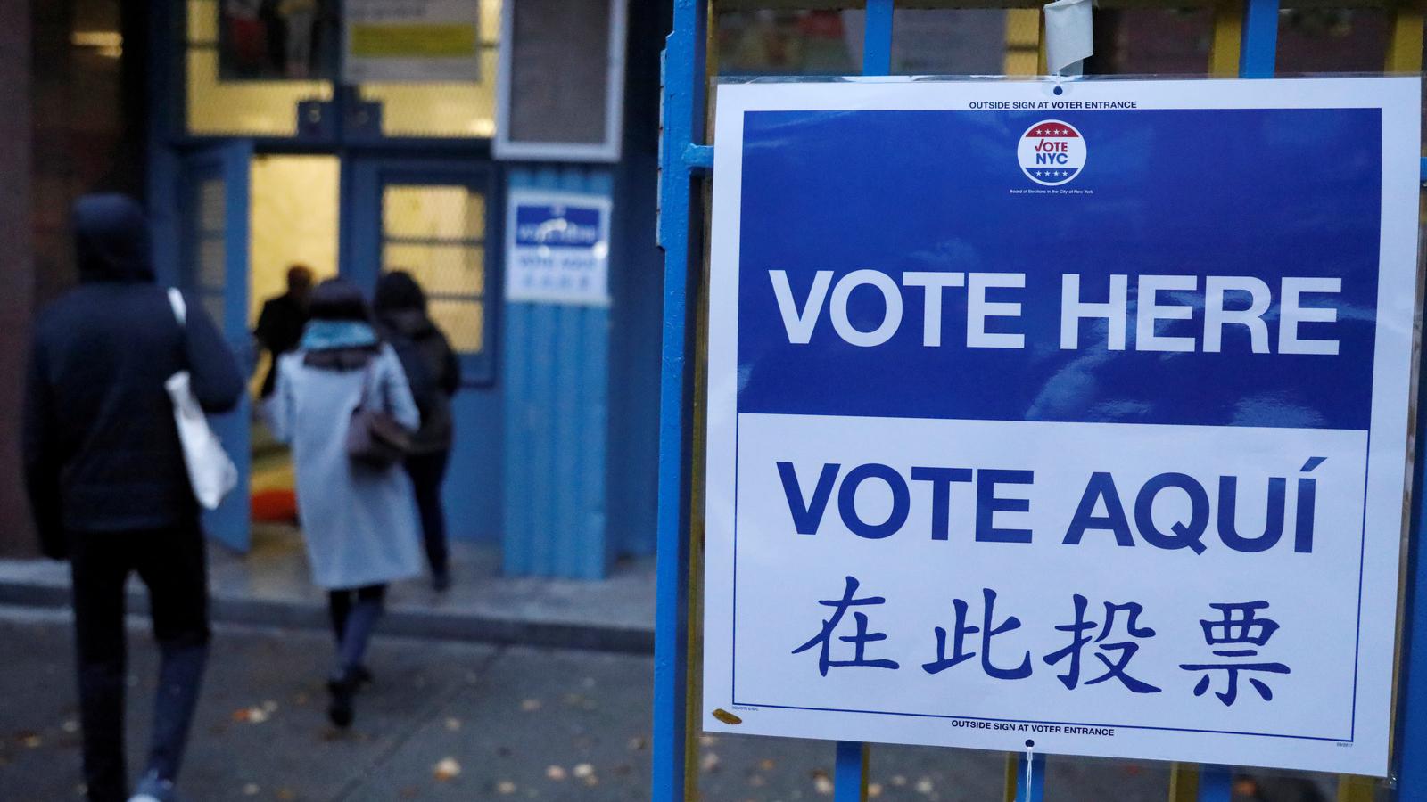 A large blue and white sign reads "Vote Here" in Spanish, Chinese and English. 
