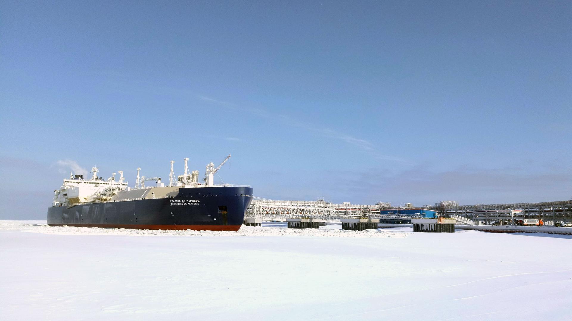 A large oil tanker docks amid ice and snow in the Arctic. On the side, the ship's name is written in Russian characters.