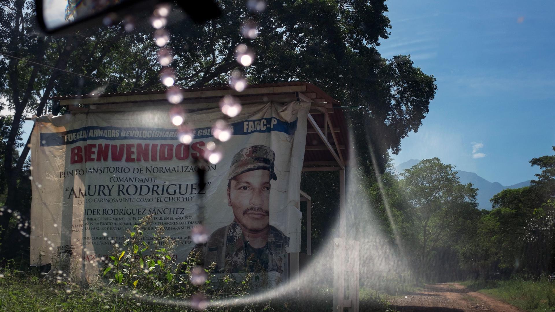 A sign seen through a windshield says "Welcome." It is marking the entrance to a FARC camp in Colombia. 