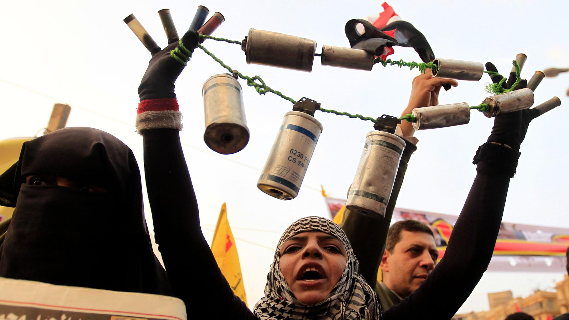 A person holds tear gas canisters and shot guns shells all tied on to a string