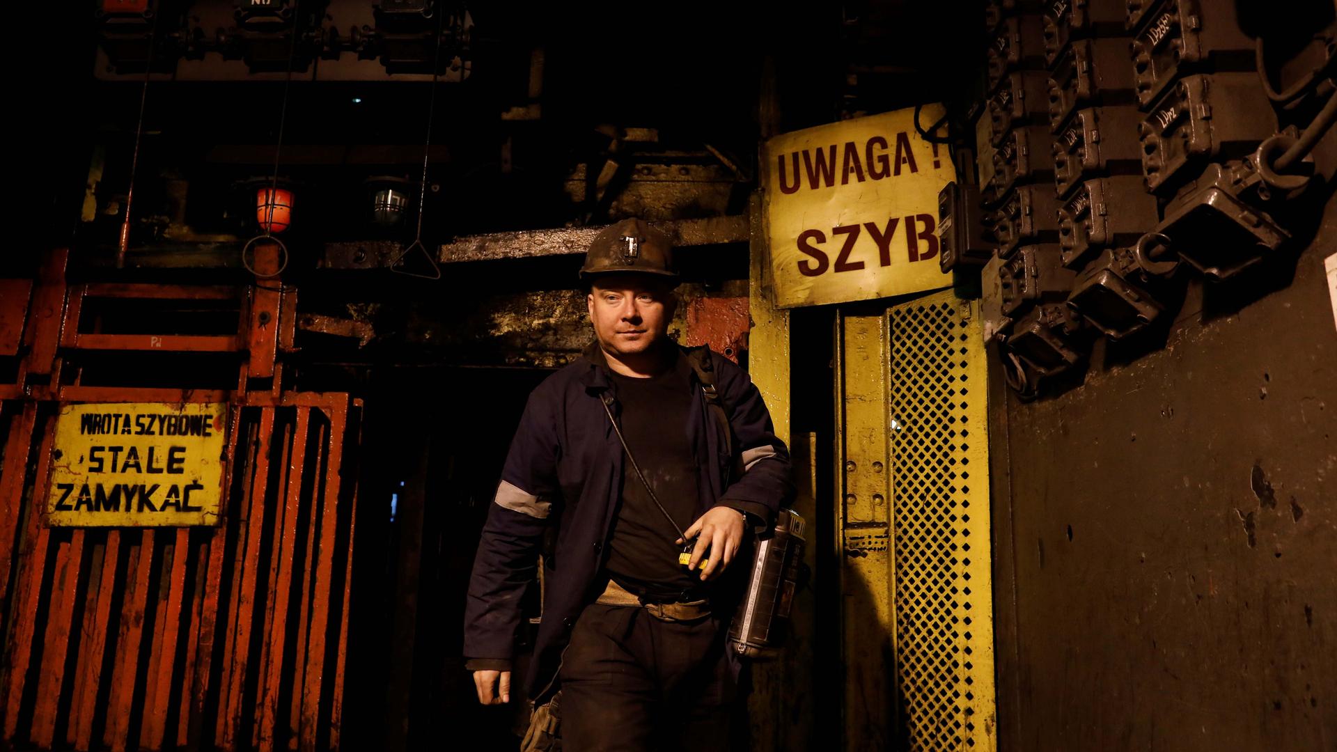 A man in mining gear exits a shaft. Signs in Polish flank the opening. 