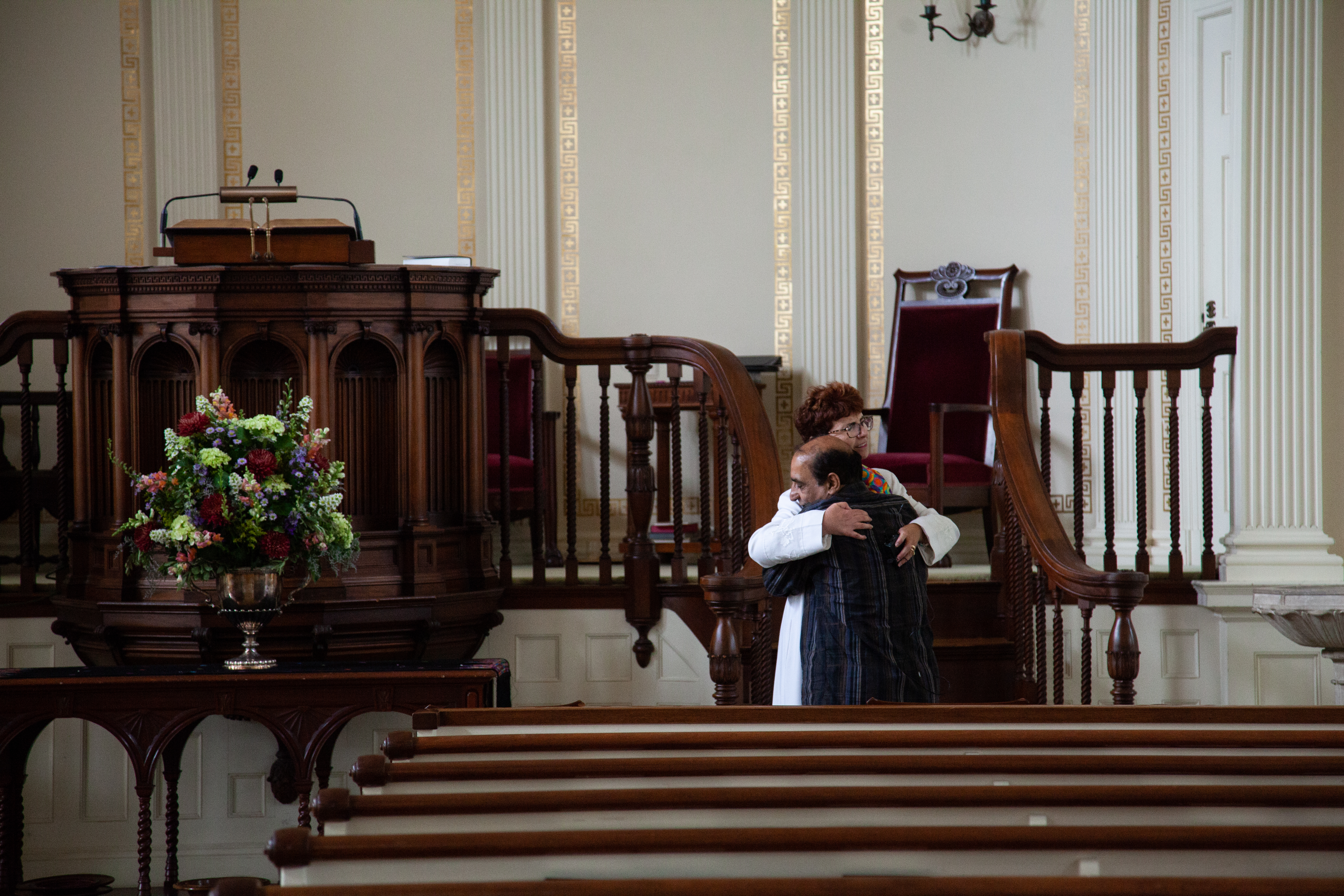 man hugging woman pastor in front of tall altar