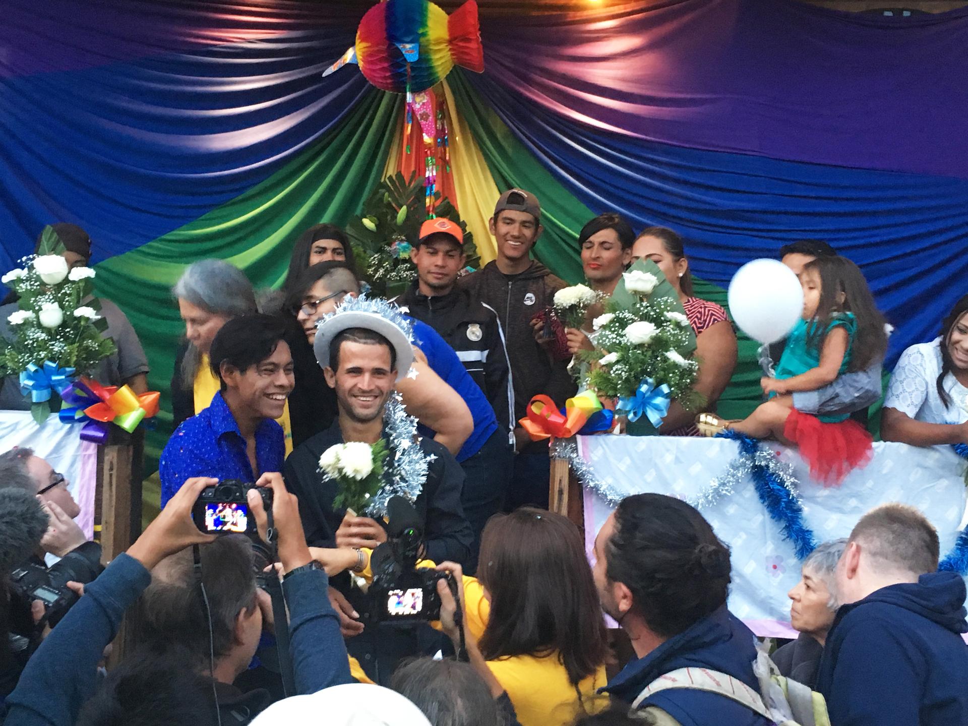 One of seven LGBTQ couples that got married in Tijuana, Mexico pose for a picture with an LGBTQ rainbow flag behind them 