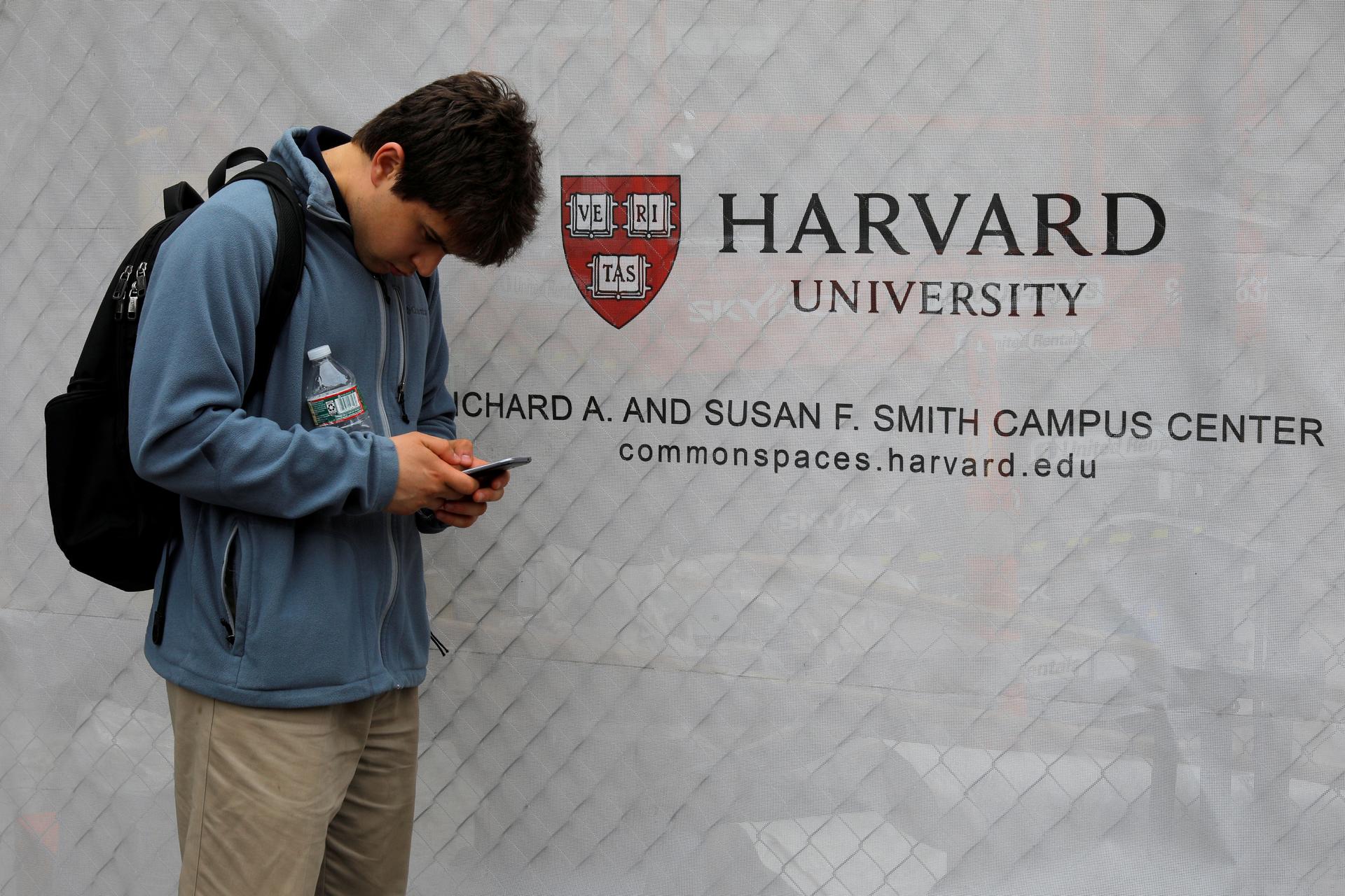 man in front of Harvard University sign looks at phone