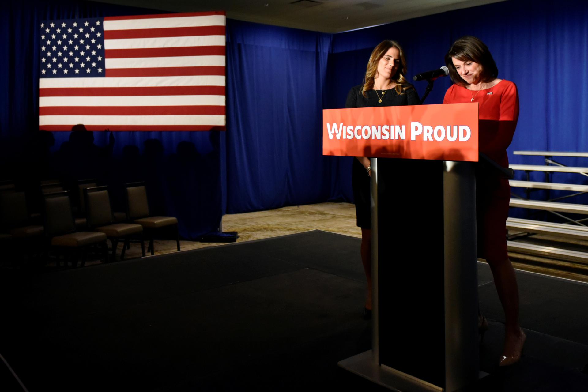 Two women stand at podium, sign reads, "Wisconsin Proud"
