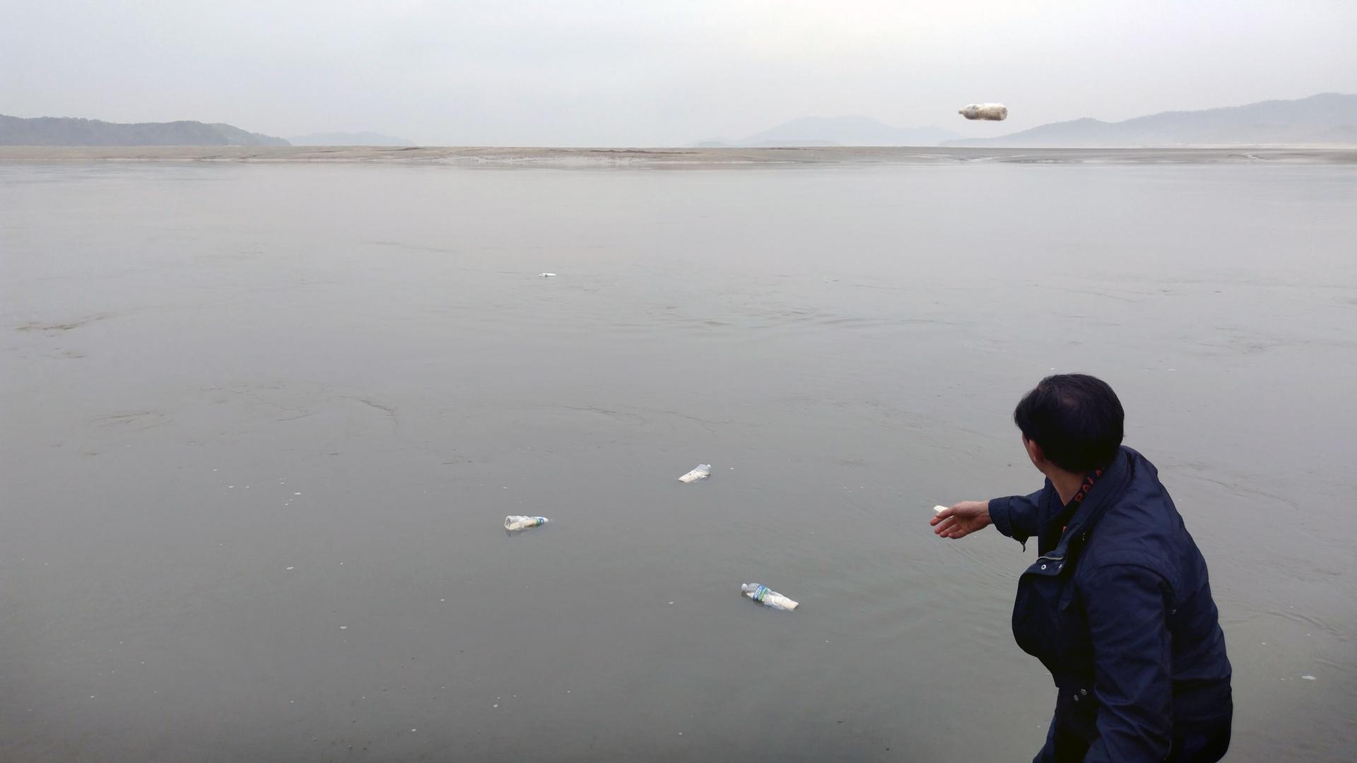 A man throws a plastic water bottle into a dark gray sea