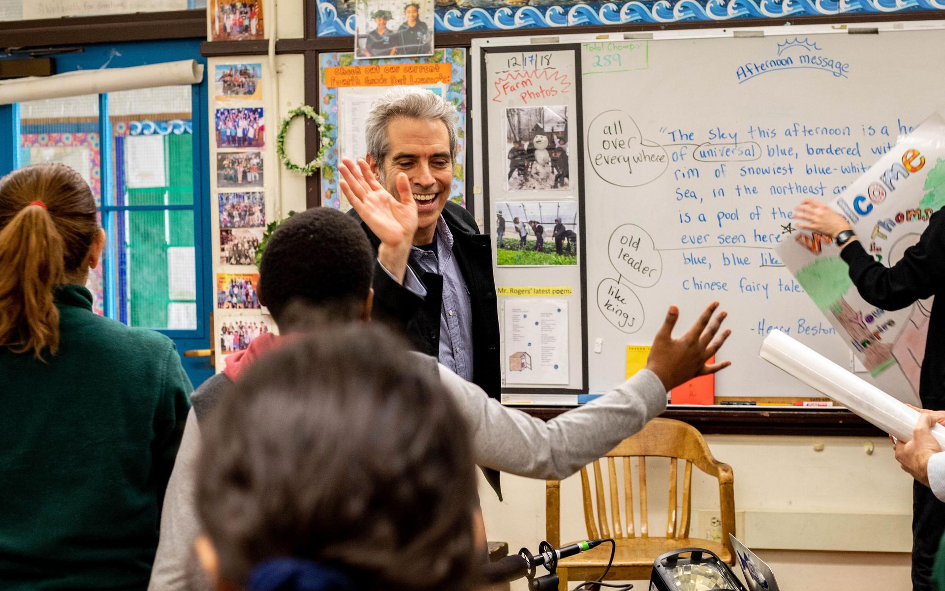 A man high fives a child in a school classroom.