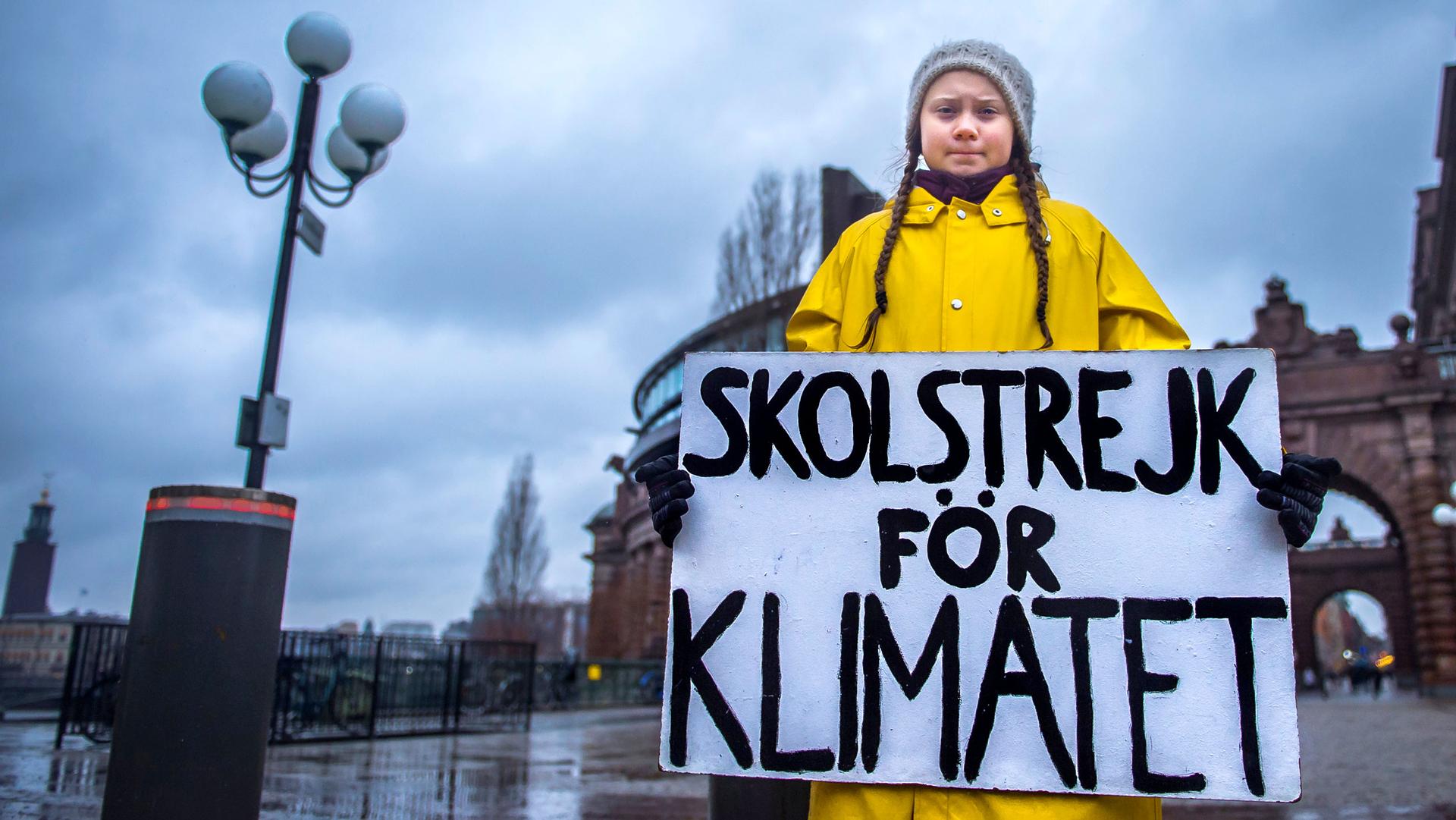 A young girl stands in front of a government building holding a sign in Swedish. Translated, it says: 