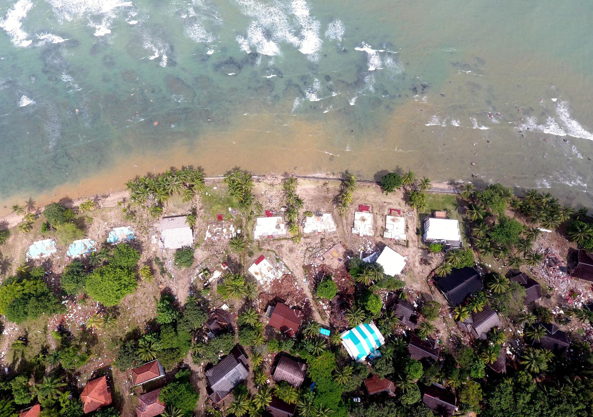 An aerial image shows buildings along a coastline. Those close to the water are destroyed.