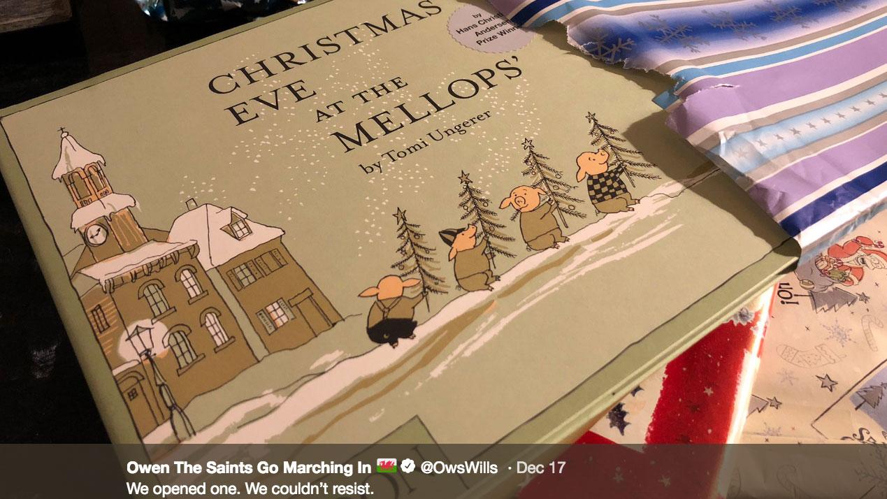 A book is sitting in torn Christmas paper. The title of the book is "Christmas Eve at the Mellops" and a photo caption underneath says "We opened one. We couldn't resist."