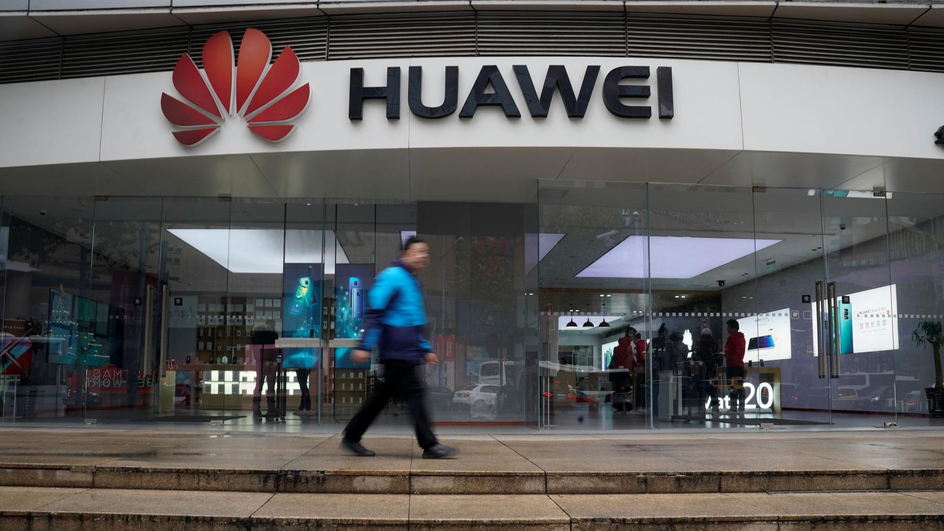 A man is shown walking by the red Huawei logo in a motion blur at a shopping mall in Shanghai, China.