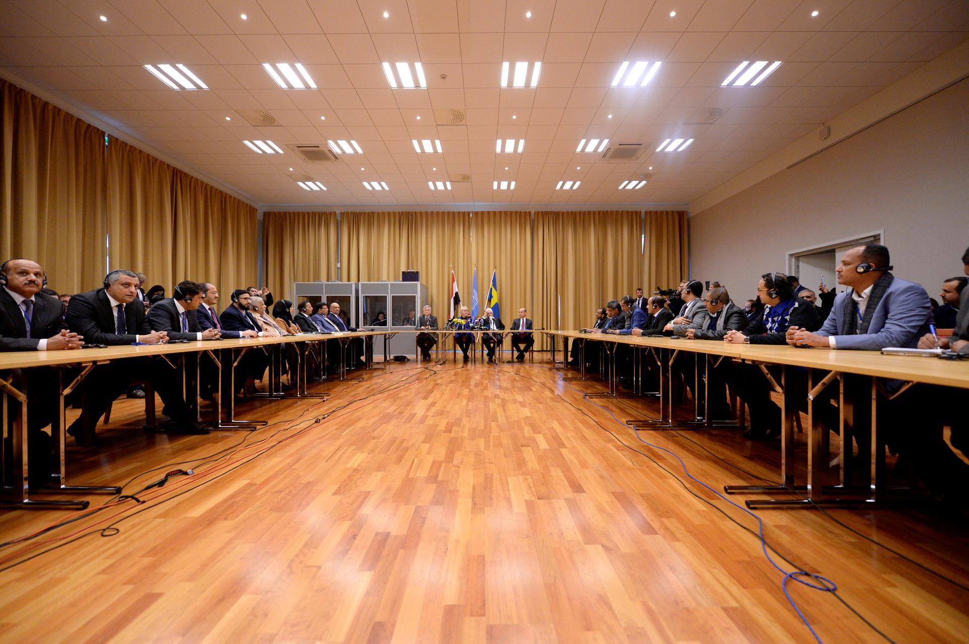 delegates sit across each other in a large room with a wood floor 