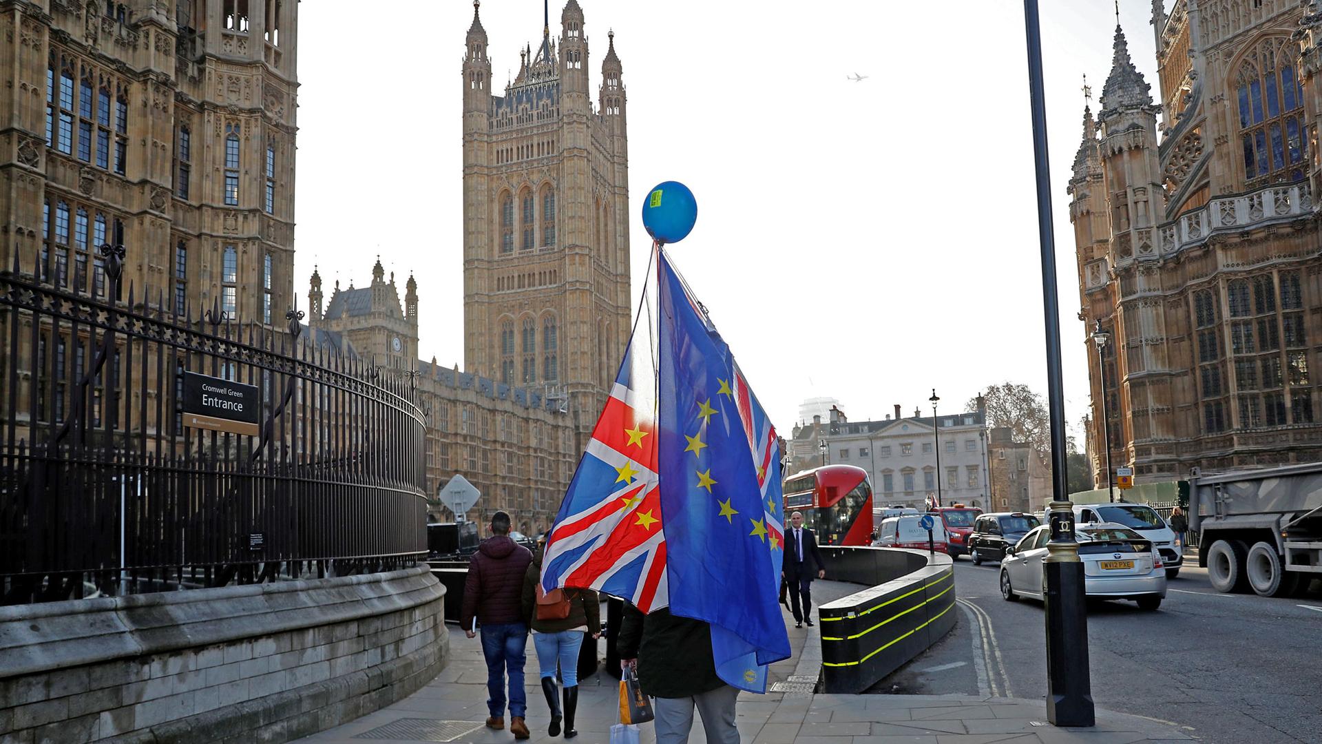 An person is show walking away from the camera carrying both British and EU flags .