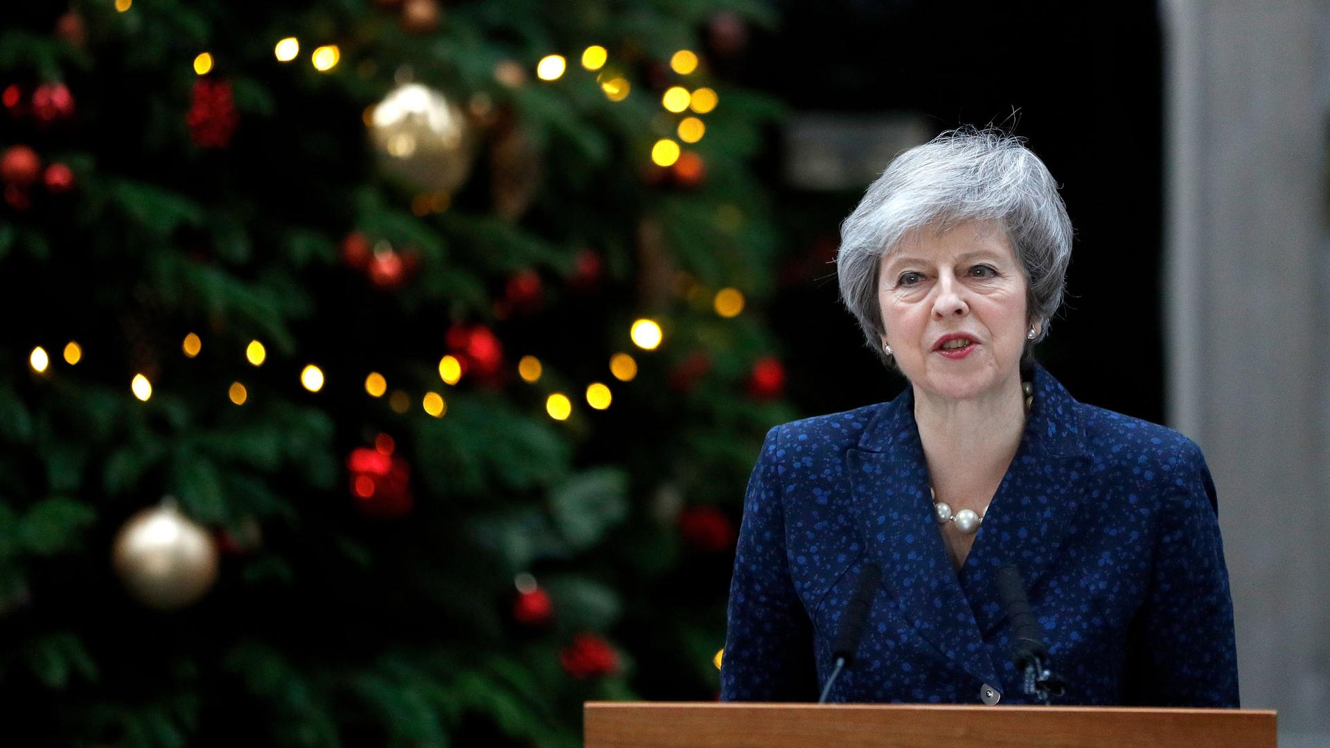 Britain's Prime Minister Theresa May is shown standing at a podium with Christmas decorations behind her.