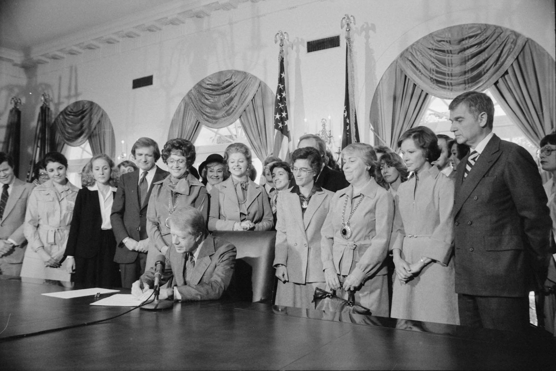 Jimmy Carter sitting down with several women standing behind him 