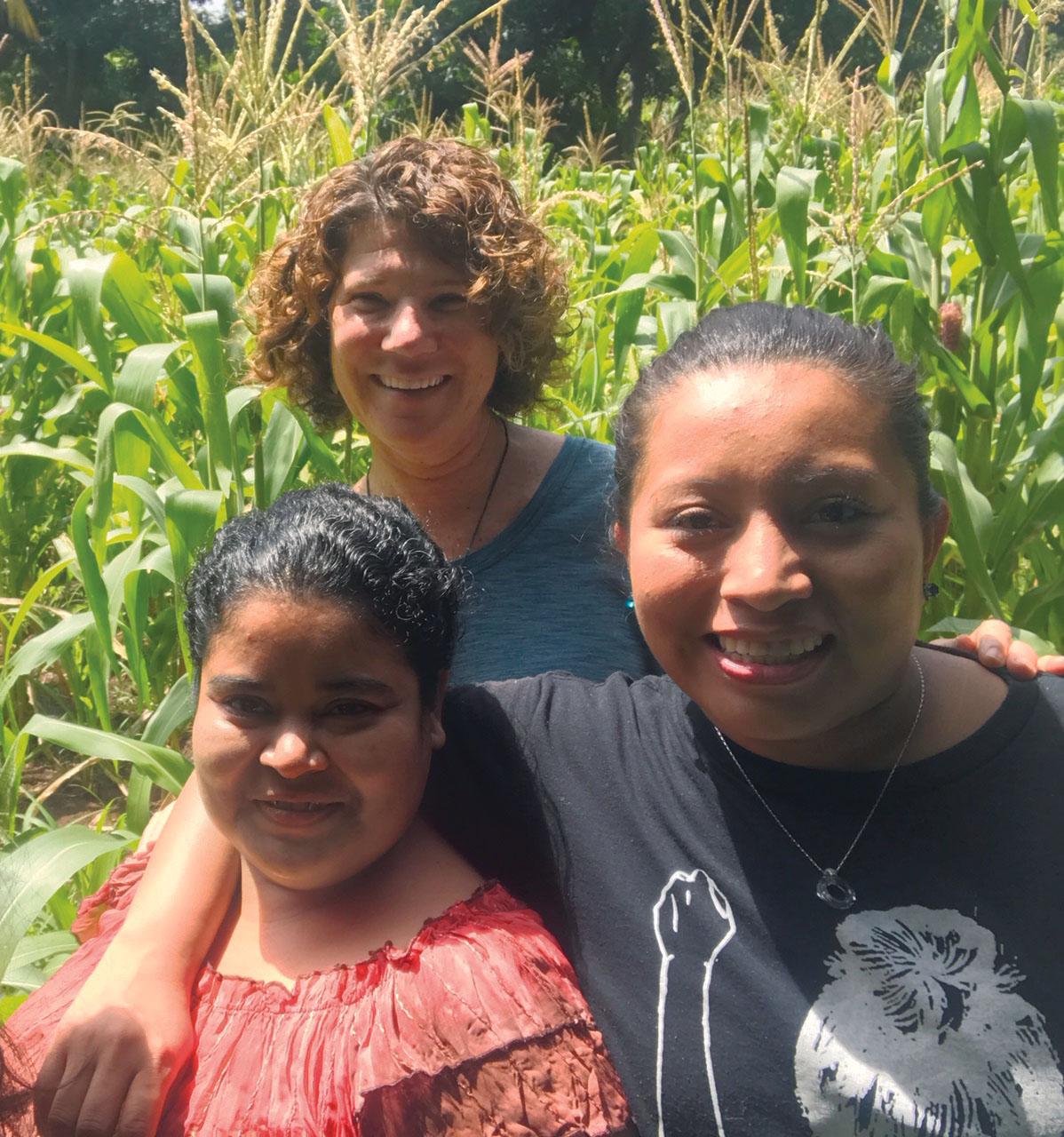three women standing closely in front of a field of corn