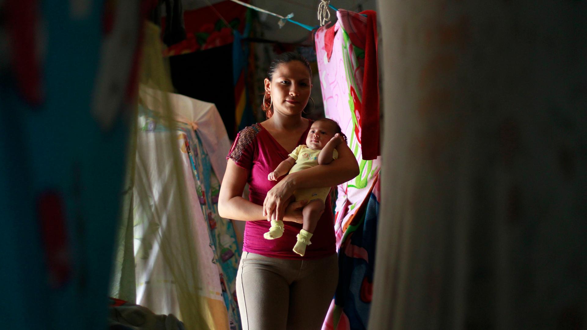 a female prisoner holds her baby in a room with laundry hanging 