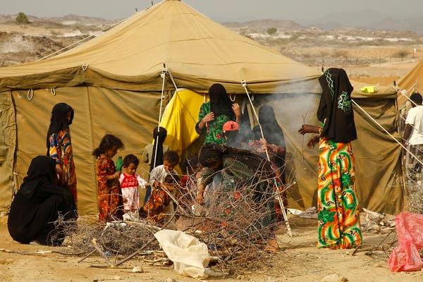 Yemen women stand near a tan tent next to a pile of fire wood.