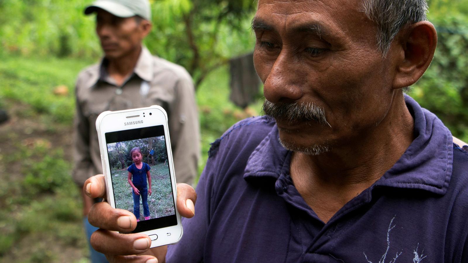 A man holds a phone with a picture of his granddaughter. 