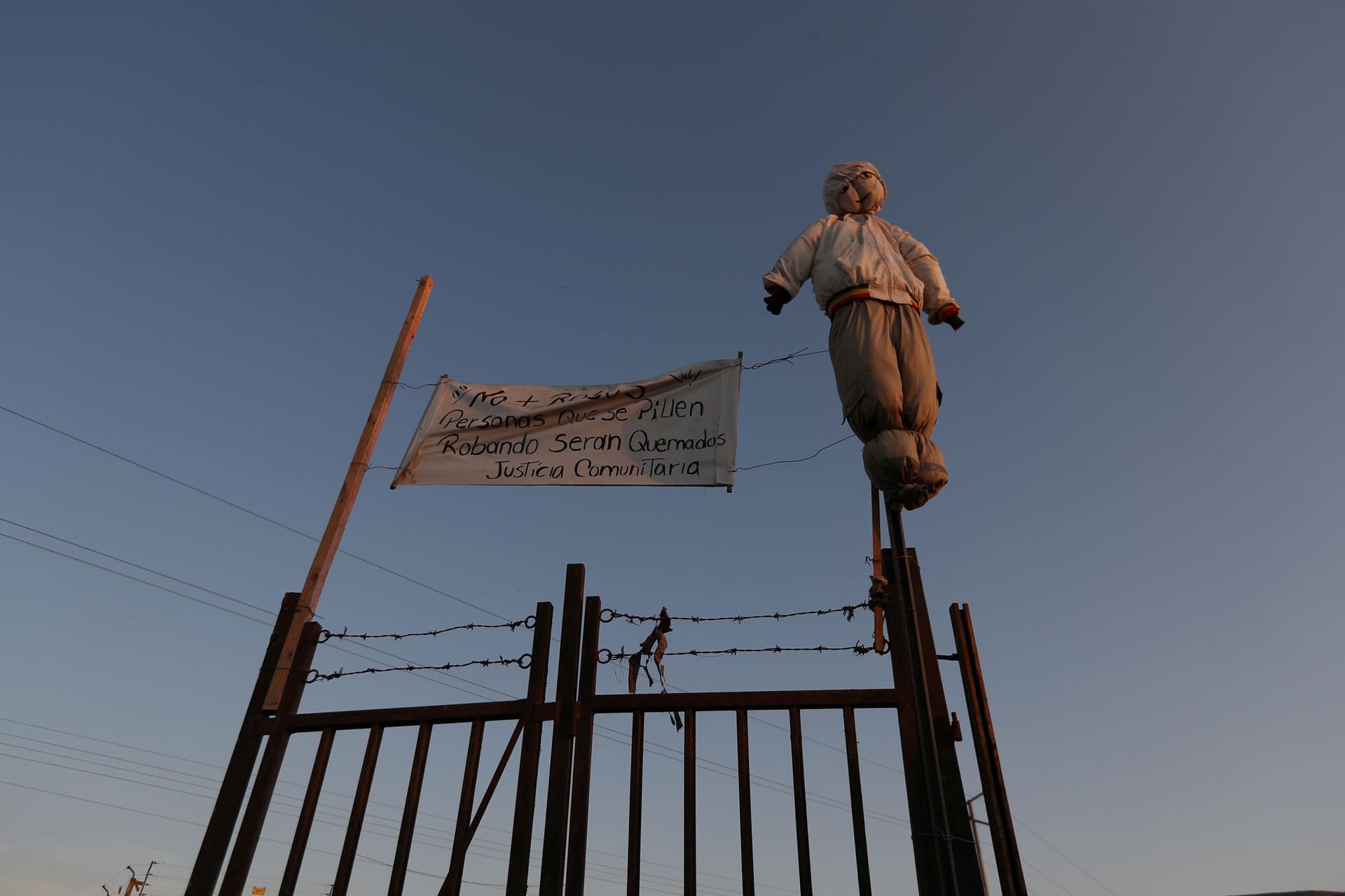 A stuffed effigy is shown hangs at a fence with barbed wire and a sign reading “No more robberies. People caught stealing will be burned. Community justice.”