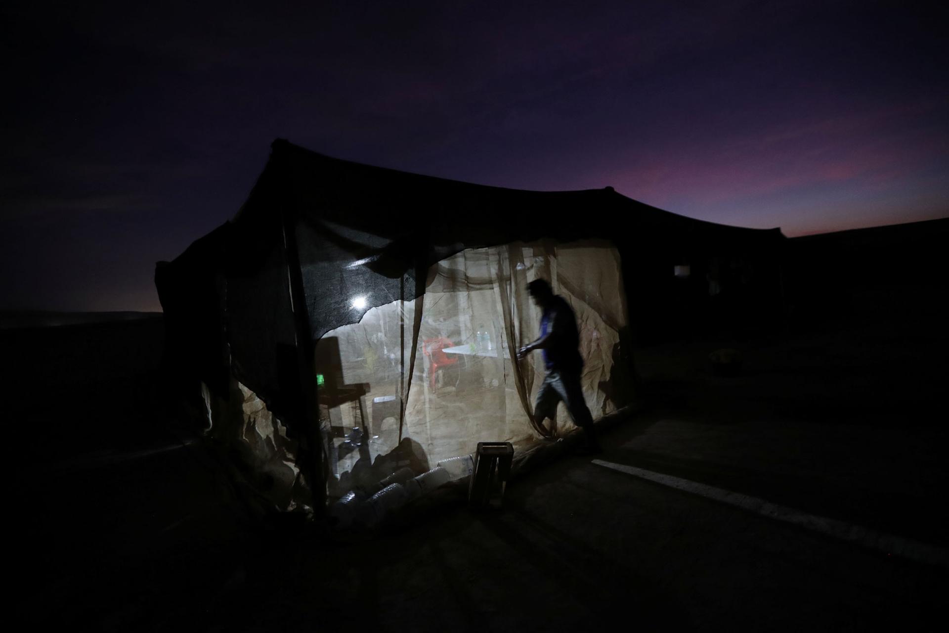 In this photo taken at night, a stand-up, mesh net-walled tent is shown lit from the inside.