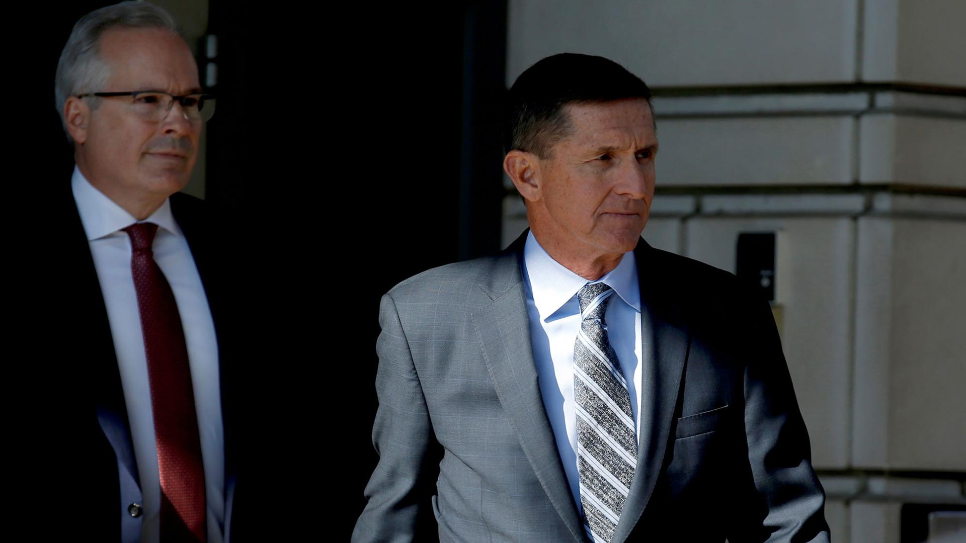 Former US National Security Adviser Michael Flynn is shown departing US District Court wearing a grey suit and striped tie.