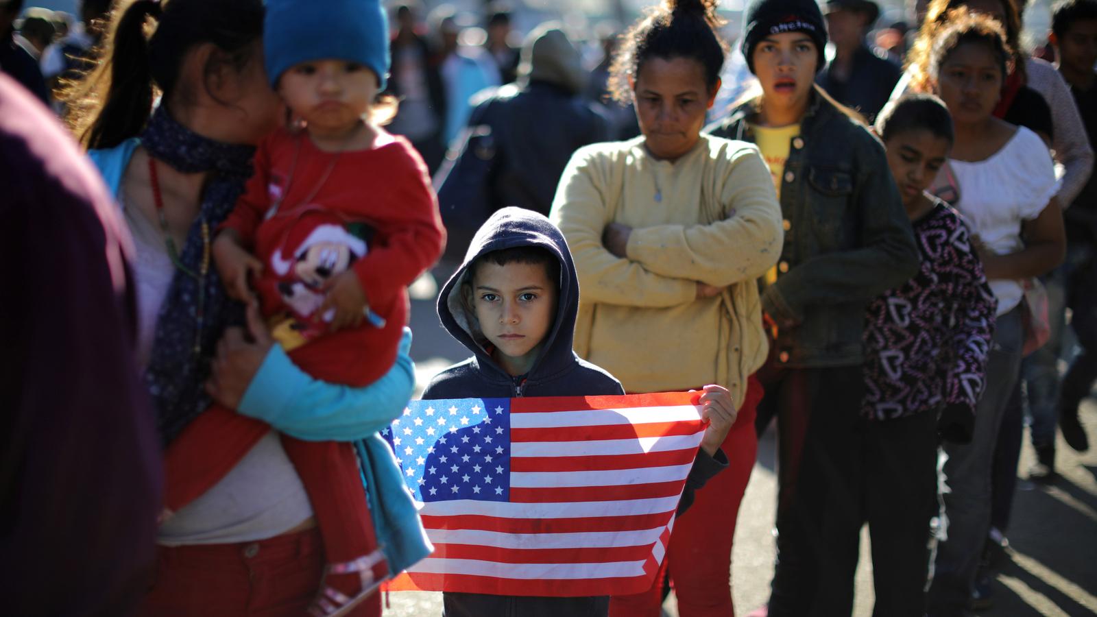 Mother with her son, holding a US flag, waits in line for food.