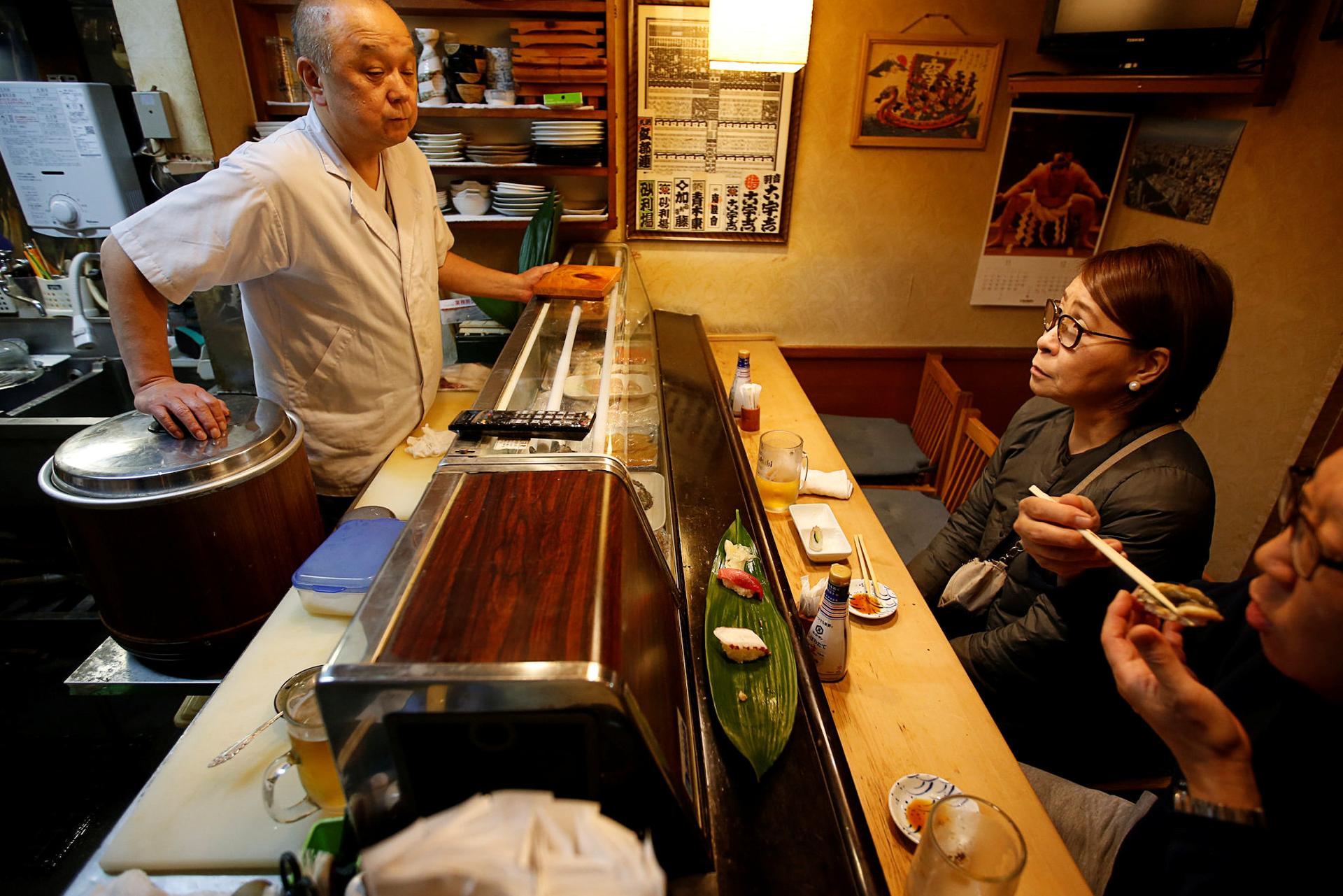 Chef chats with customers at sushi bar.