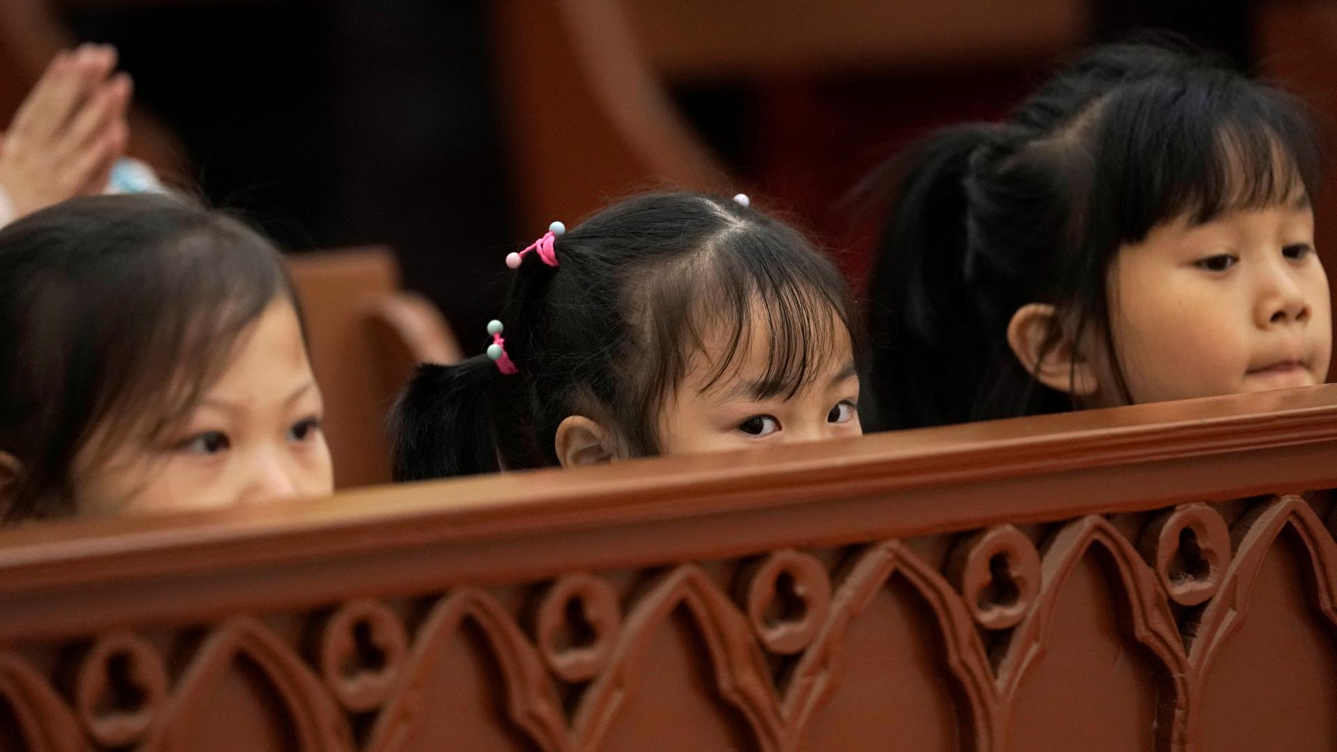 Three girls peer over the pew in church in China. 