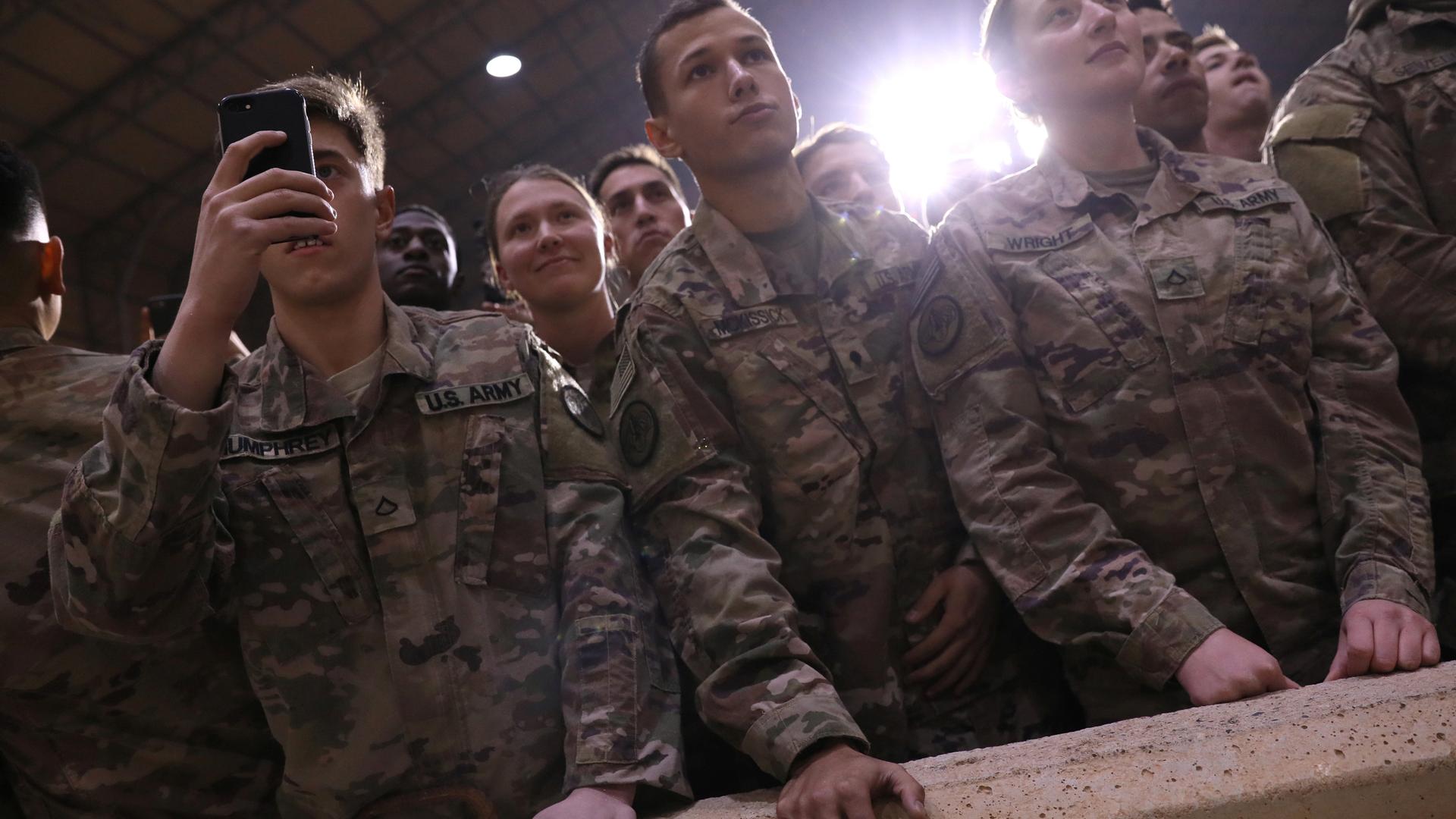 US soldiers watch Trump give a speech in Iraq at US airbase.