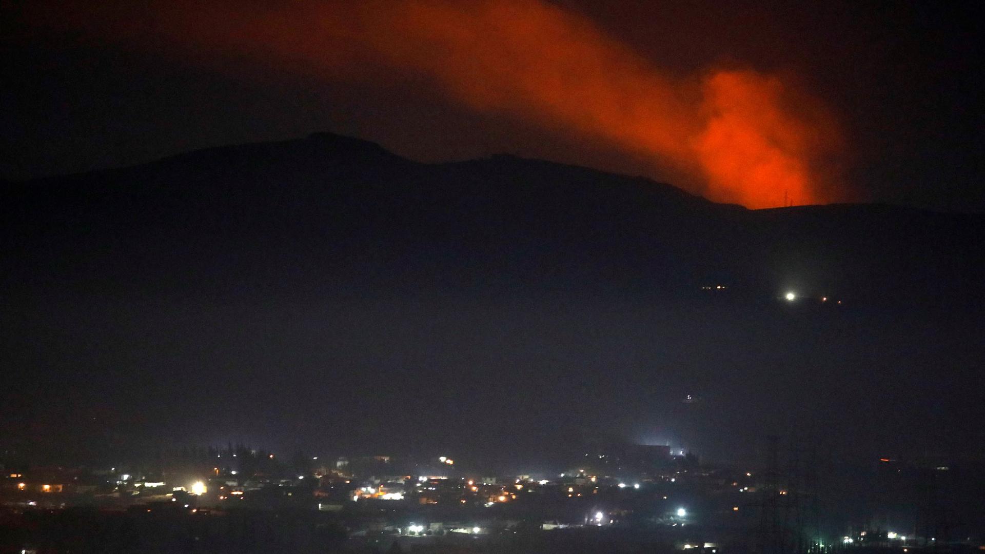 Smoke is shown with red backlighting rising past a mountain range as seen from the Damascus, Syria, countryside.