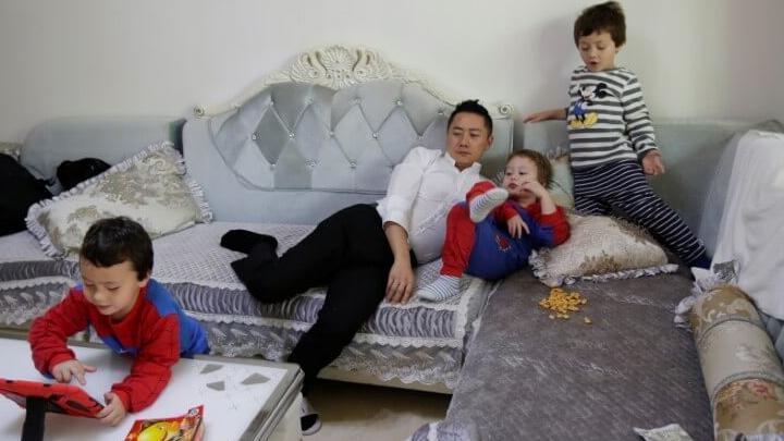 A father rests on the sofa with this three sons in China. 