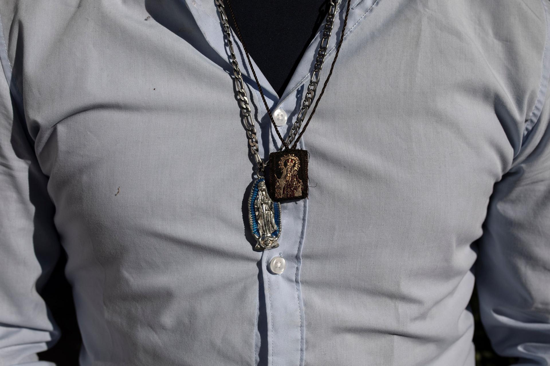 In this close-up photograph, Victor Alfonso in a blue button down shirt, wears charms depicting the Virgin of Guadalupe.