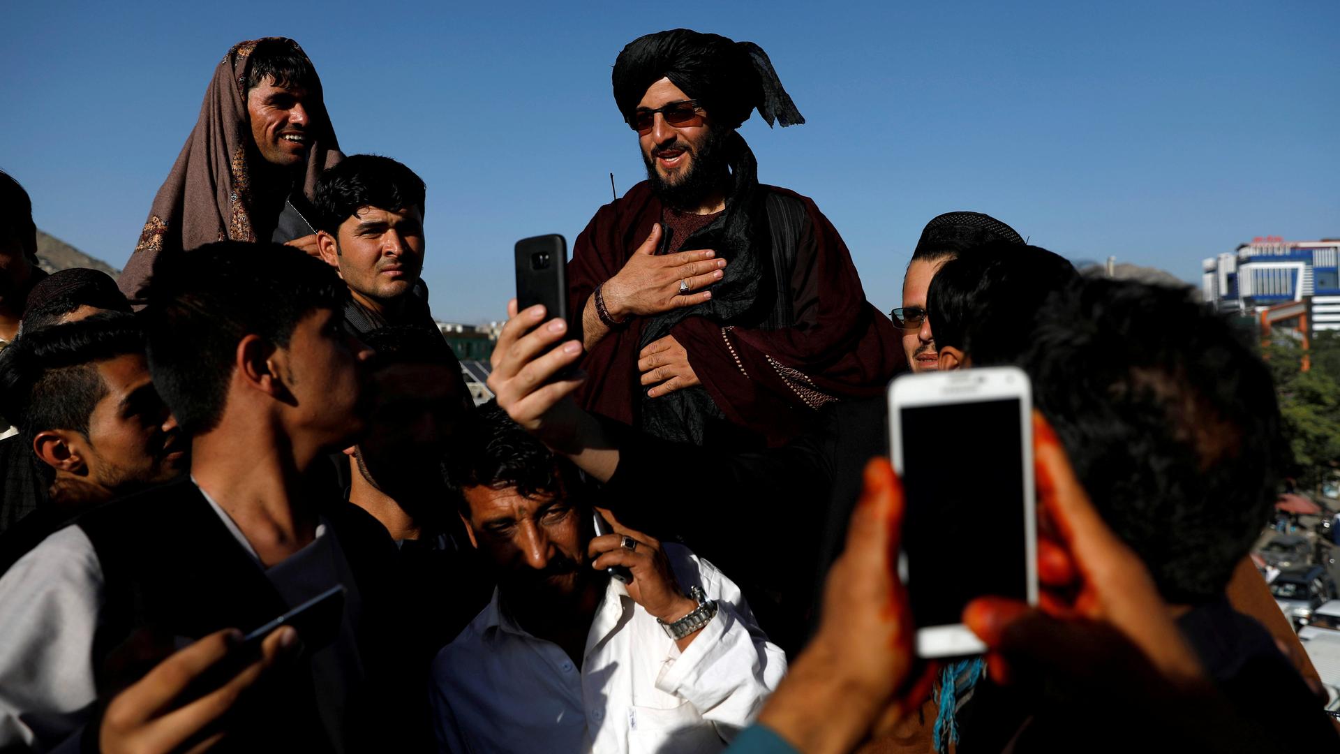 a taliban being carried on people's shoulders while others take photos