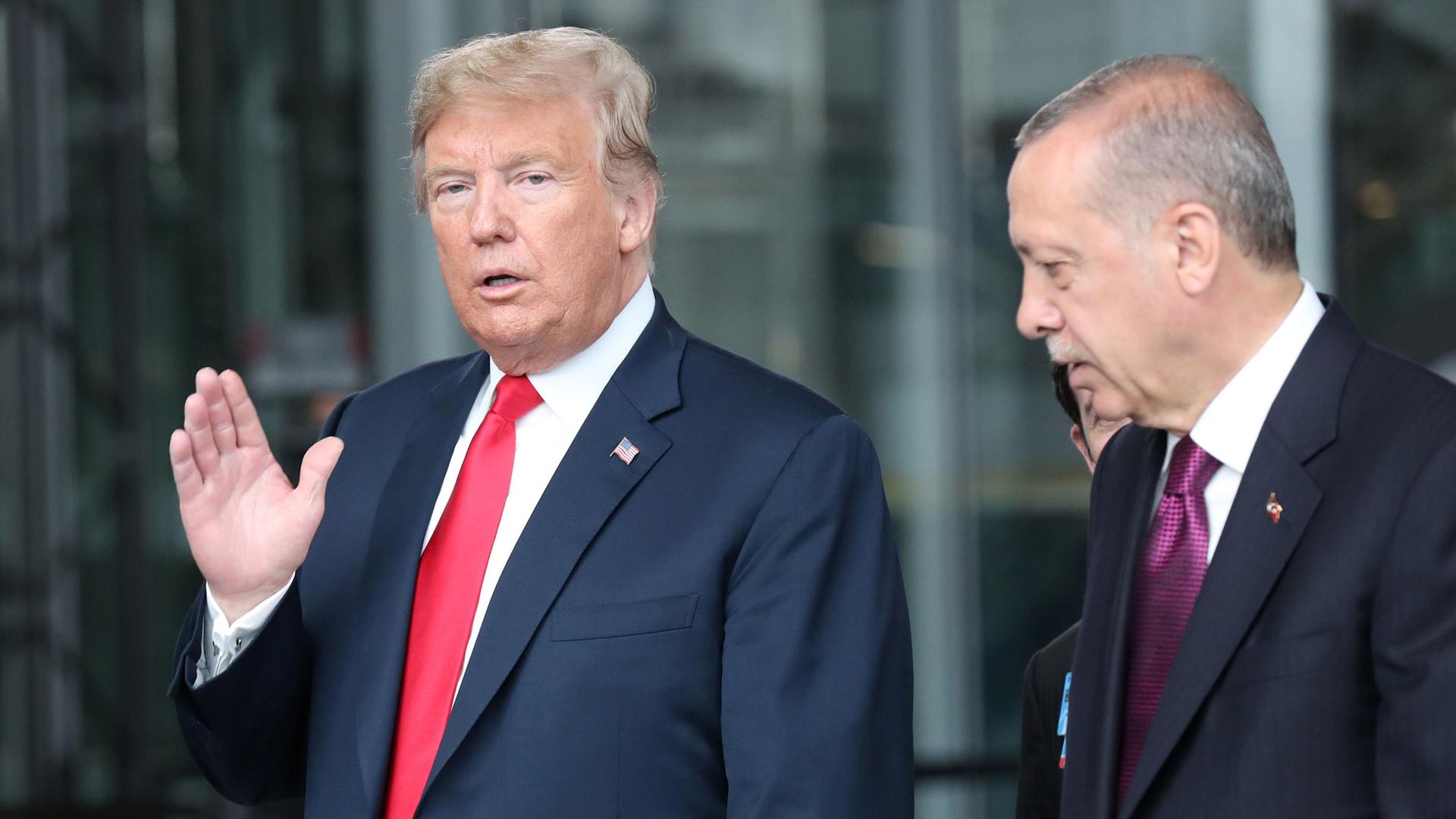 President Donald Trump is shown walking with Turkey's President Recep Tayyip Erdoğan with his right hand raised waving at the camera.